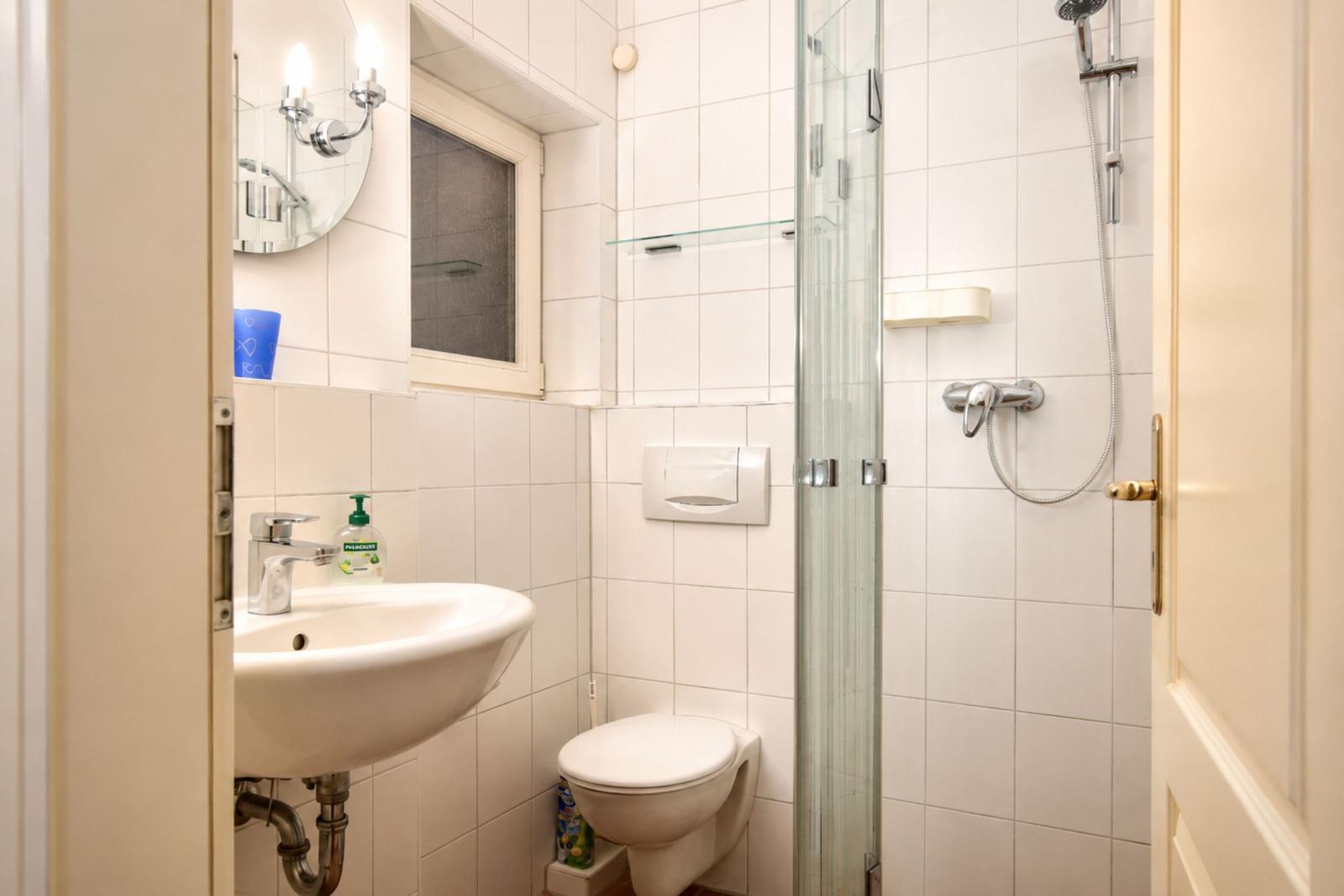 Bathroom with shower, sink, and toilet. White tiles and mirror.