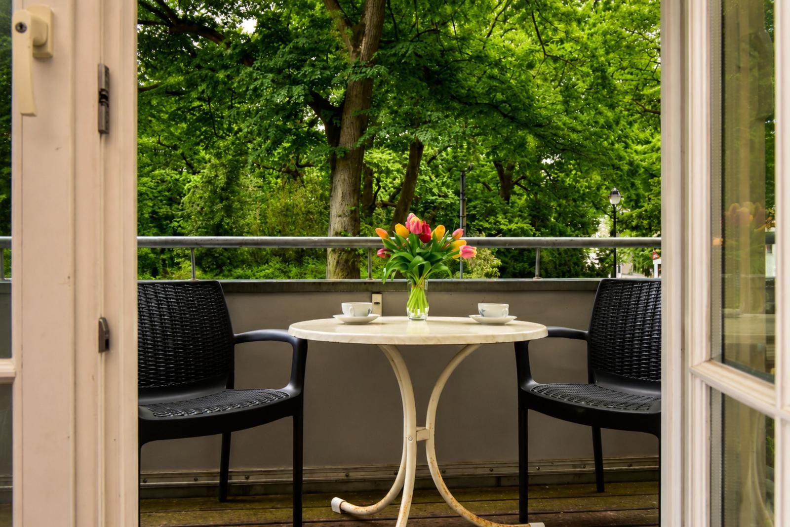Terrace with table, two chairs, and flower bouquet. View of green trees.