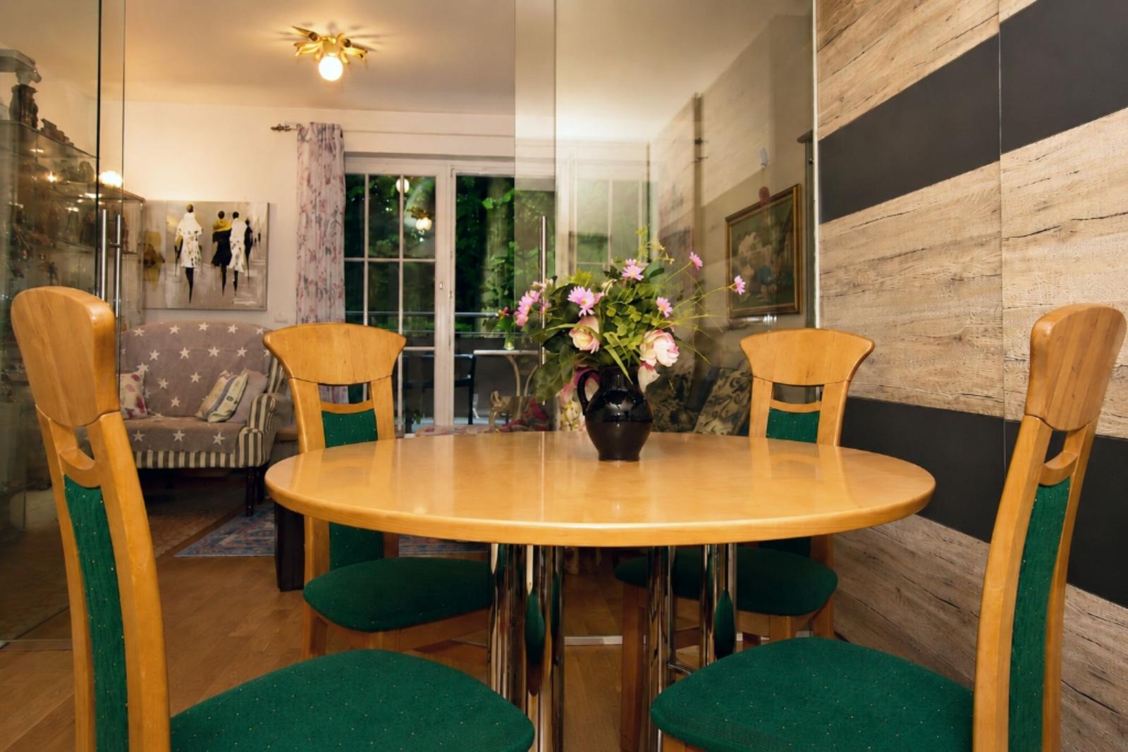 Round table with four chairs and flower arrangement. Living area with window in background.