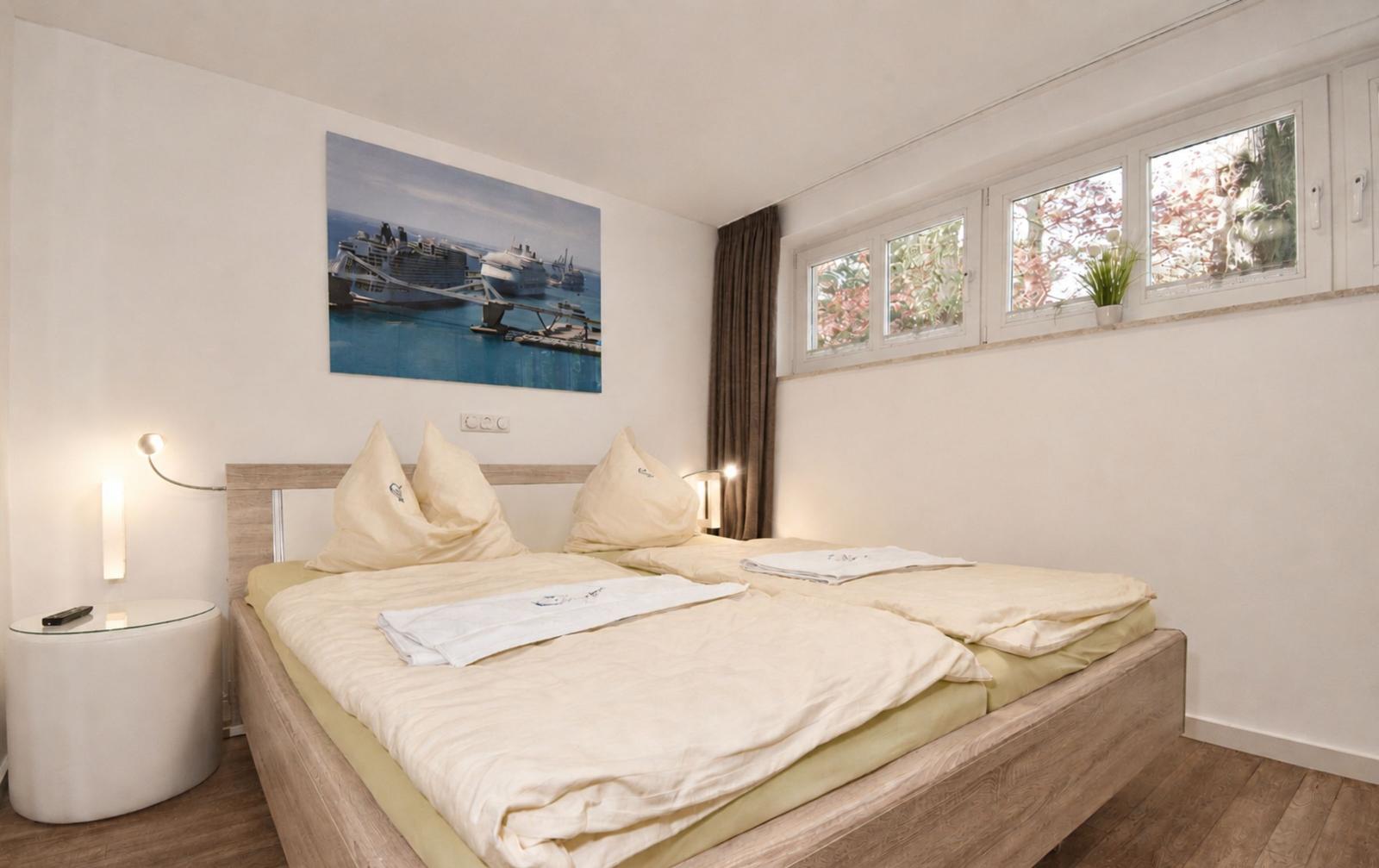 Schlafzimmer mit Doppelbett, Wandbild und Fenster mit Blick auf Bäume.