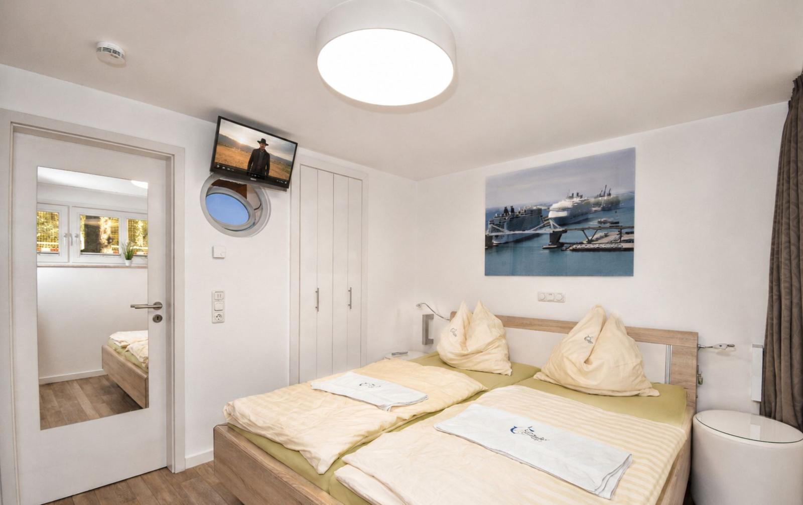 Schlafzimmer mit Doppelbett, Wandbild und TV. Tür führt in angrenzenden Raum.