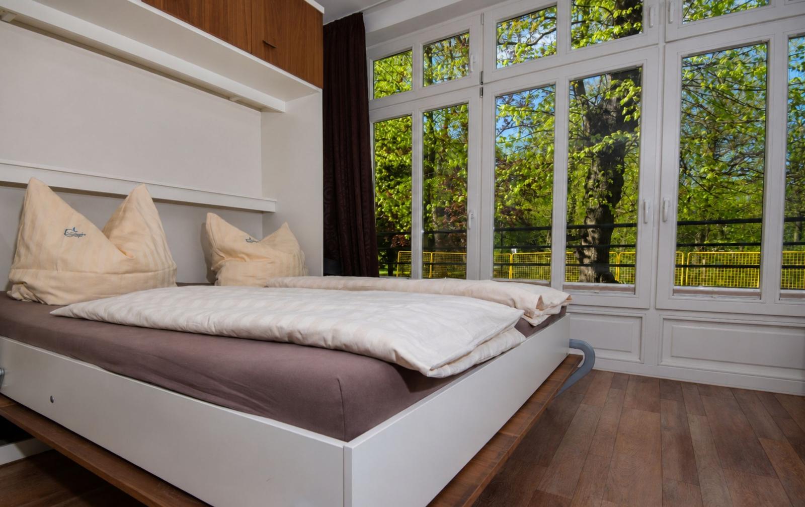 Schlafzimmer mit Bett, Fenstern und Blick auf Grün
