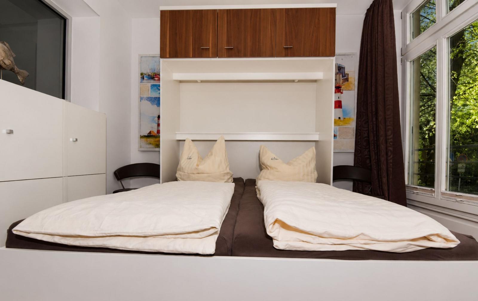 Doppelbett mit weißen Bettwäsche und Holzschränken über dem Bett.