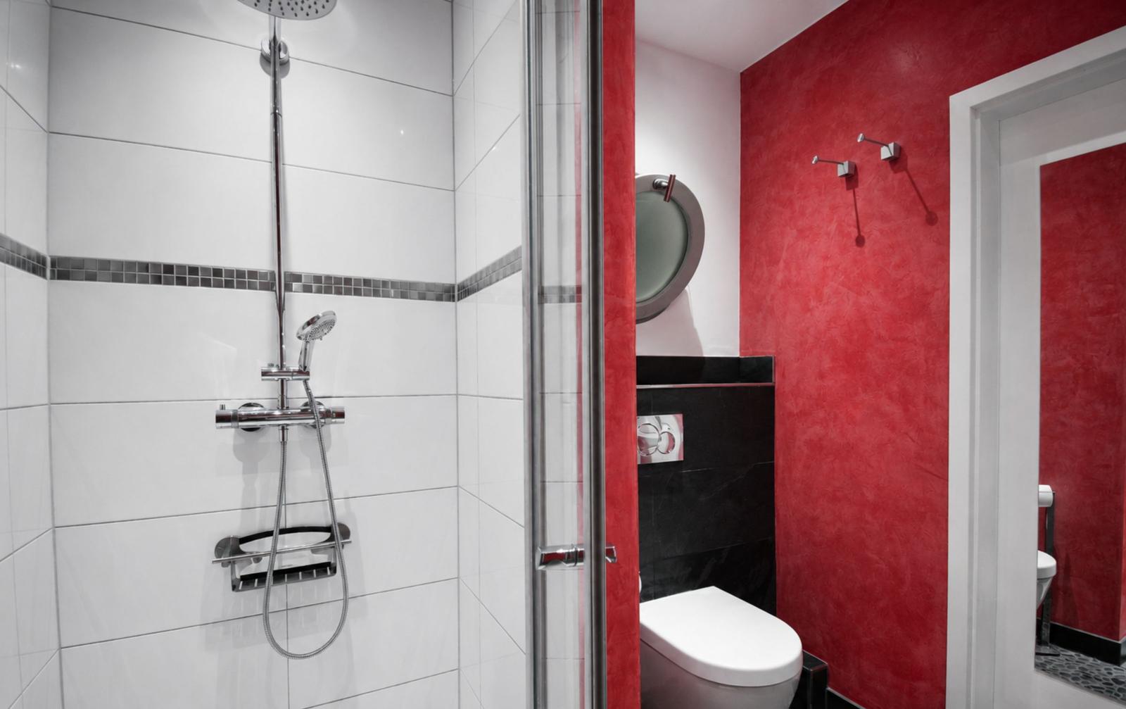Badezimmer mit Dusche, Toilette und roter Wand