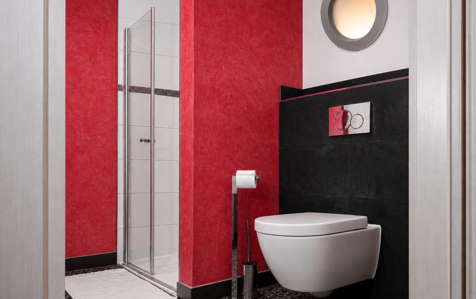 Badezimmer mit Dusche, Toilette und roten Wänden.