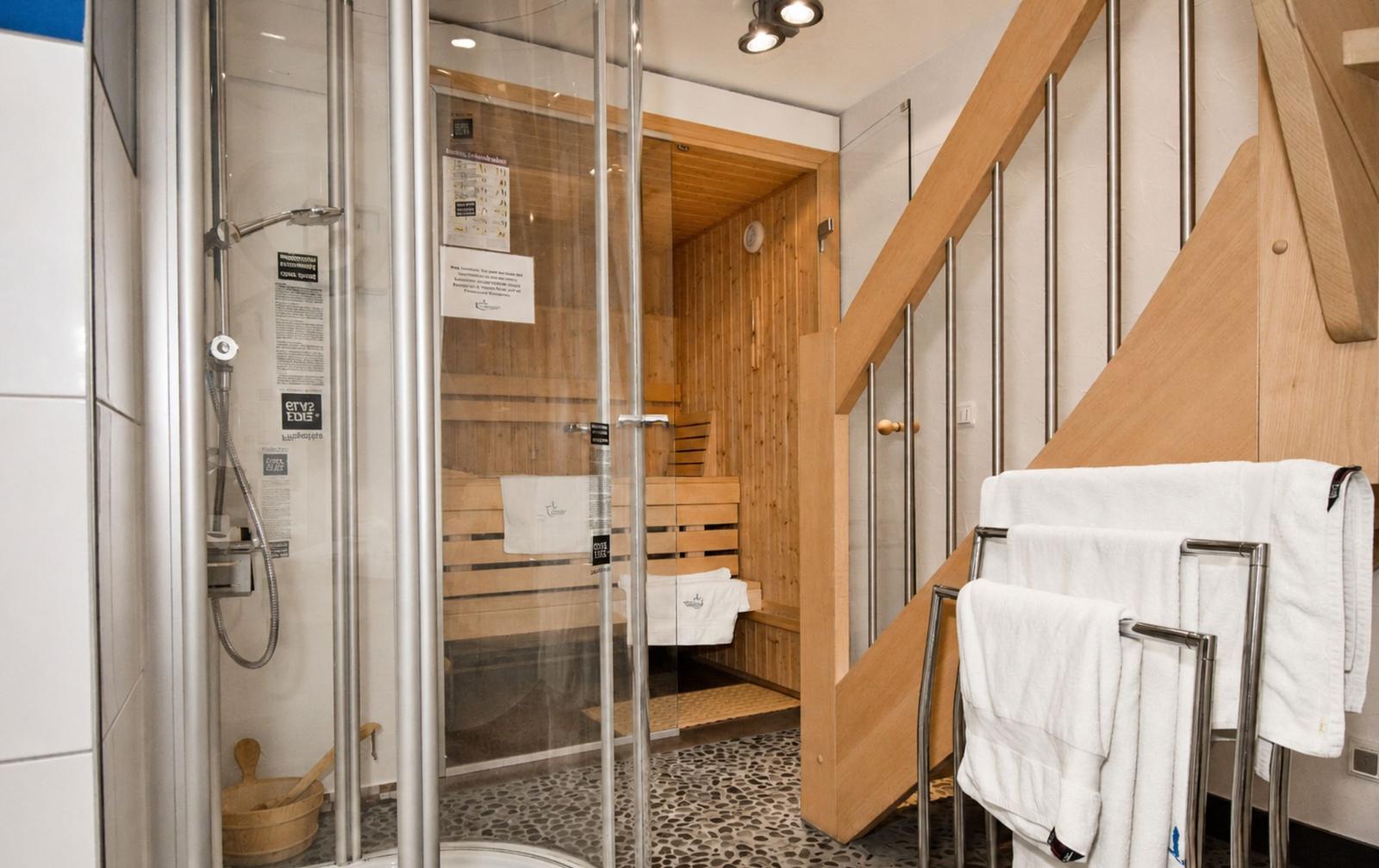 Dusche mit Glaswand und Sauna im Hintergrund. Handtuchständer mit weißen Handtüchern.