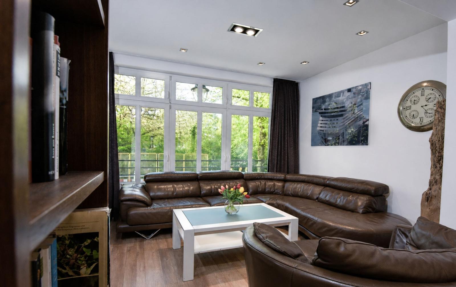 Wohnzimmer mit braunem Ledersofa, weißem Couchtisch und großen Fenstern.