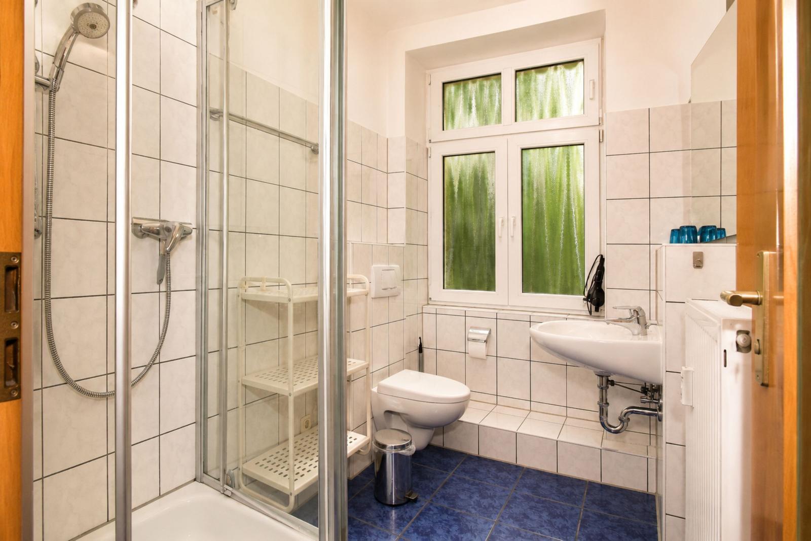 Badezimmer mit Dusche, Toilette und Waschbecken. Fenster mit grünem Vorhang.