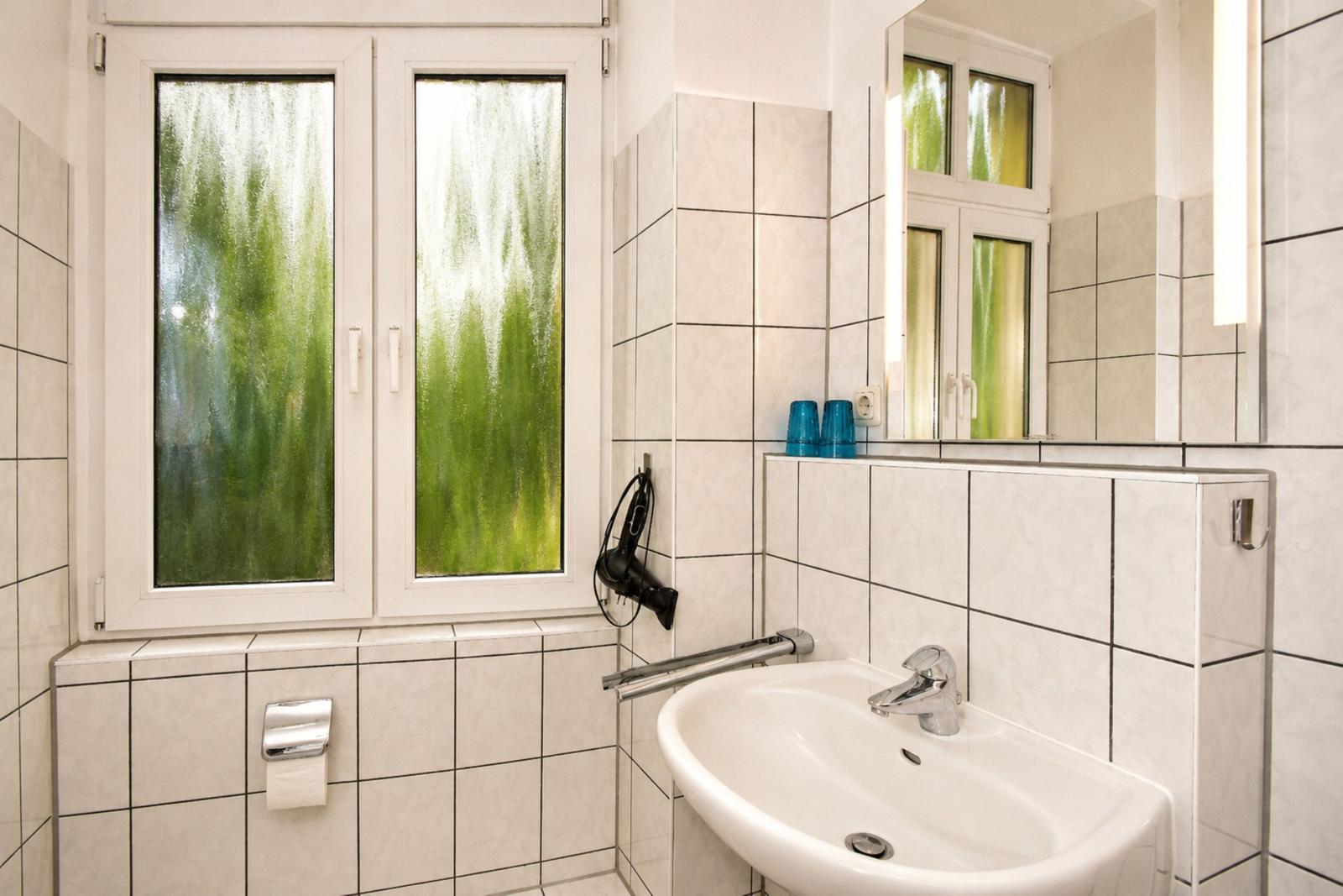 Badezimmer mit Waschbecken, Spiegel und Fenster mit grünem Glas.