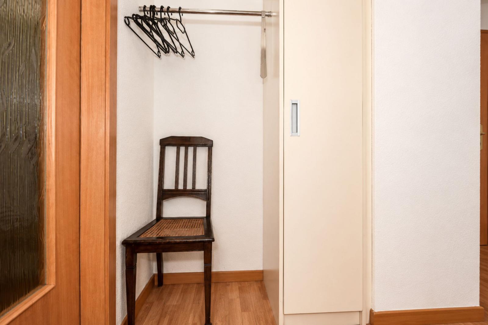 Ein kleiner Raum mit Stuhl, Kleiderständer und Schrank.