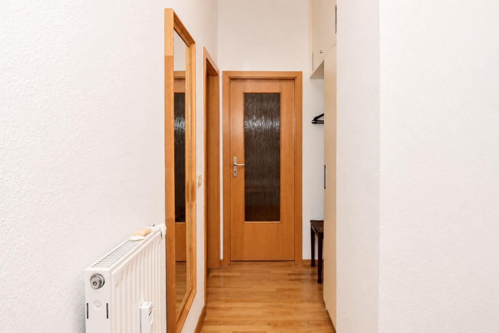 Flur mit Holztür, Spiegel und Heizkörper an der Wand.