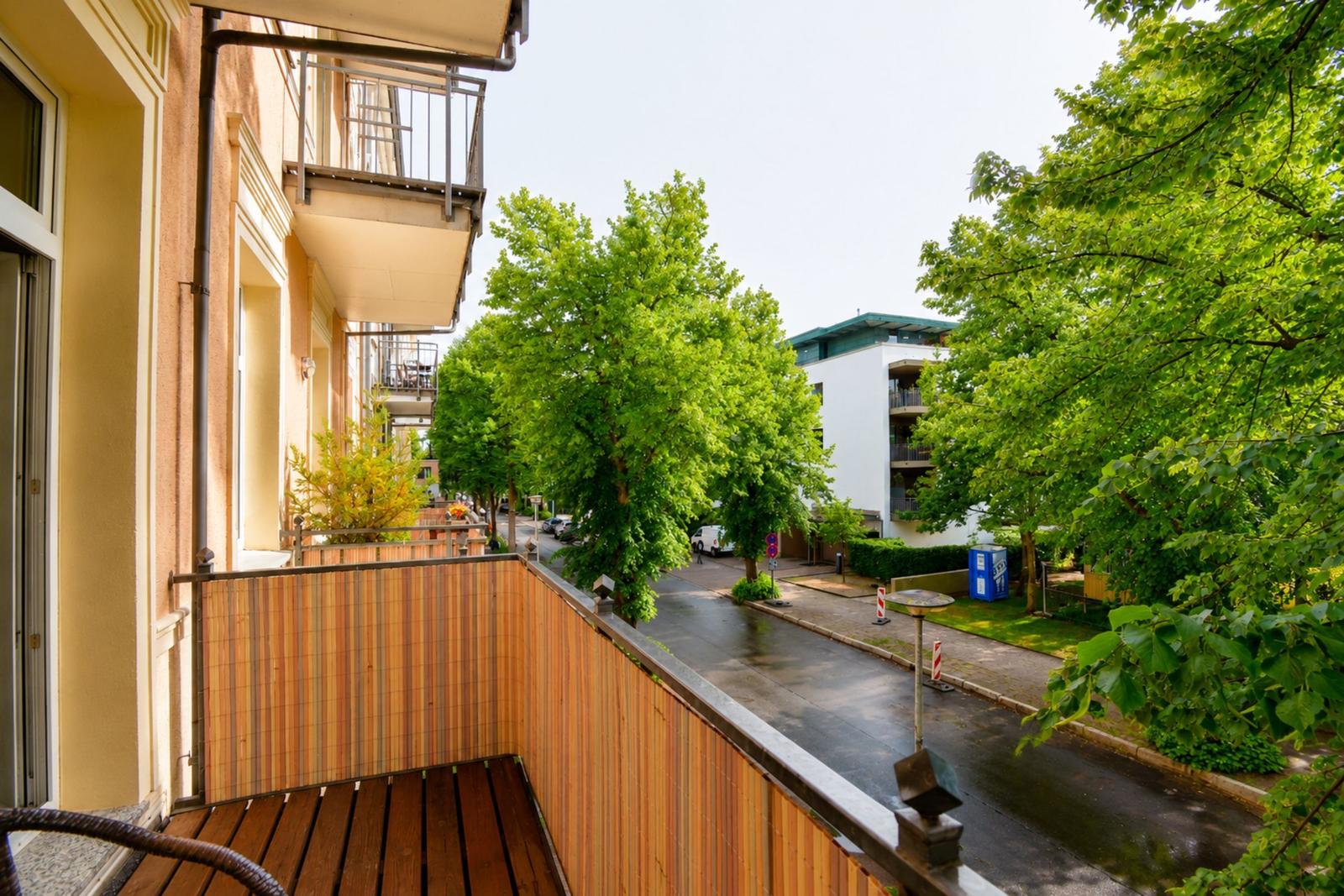 Terrasse mit Holzbelag und Blick auf grüne Bäume und Straße