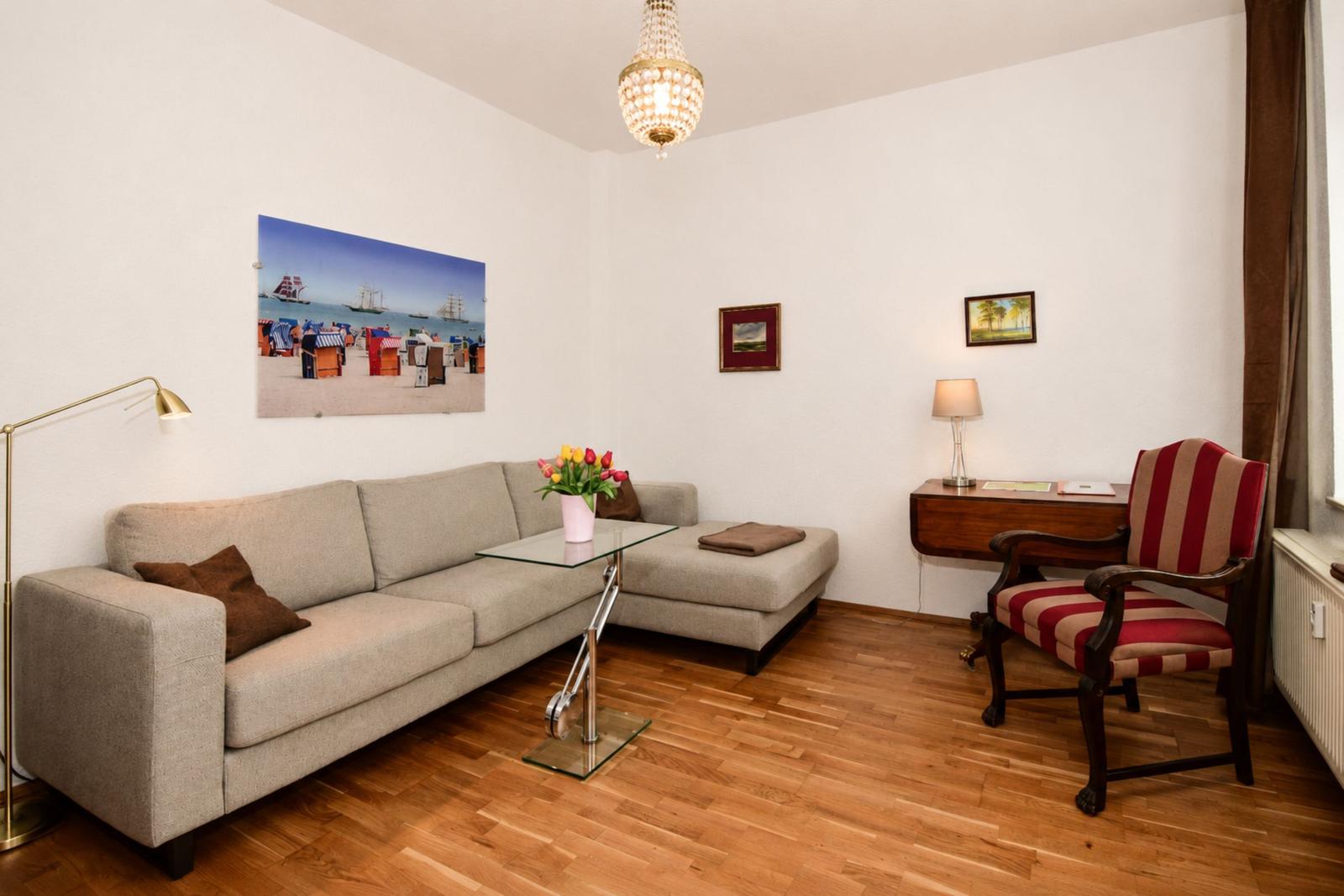 Wohnzimmer mit Sofa, Stuhl, Tisch und Wandbild. Holzboden und Kronleuchter.