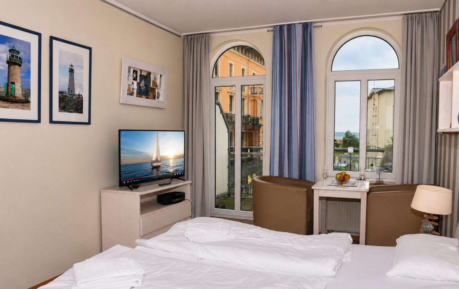Schlafzimmer mit Blick auf Balkon und Stadt. TV, Bett und Sitzgelegenheit.