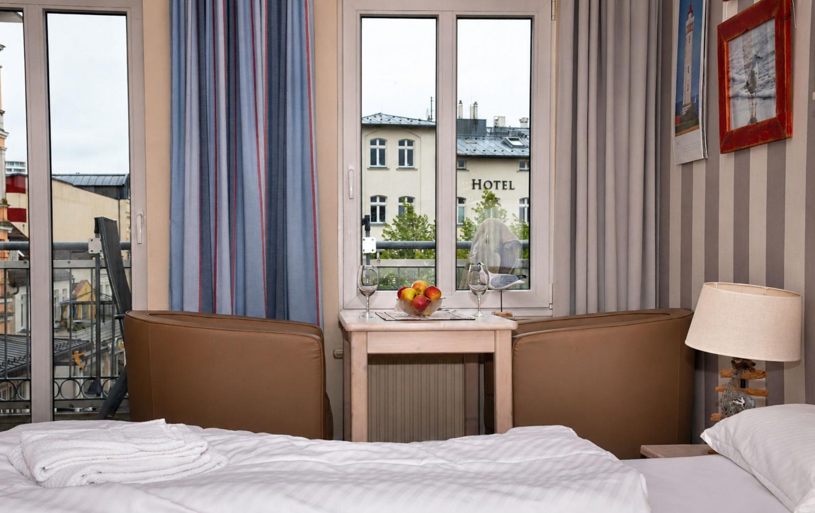 Zimmer mit Bett, Fenster und Tisch mit Obst und Gläsern. Blick auf Hotel und Balkon.