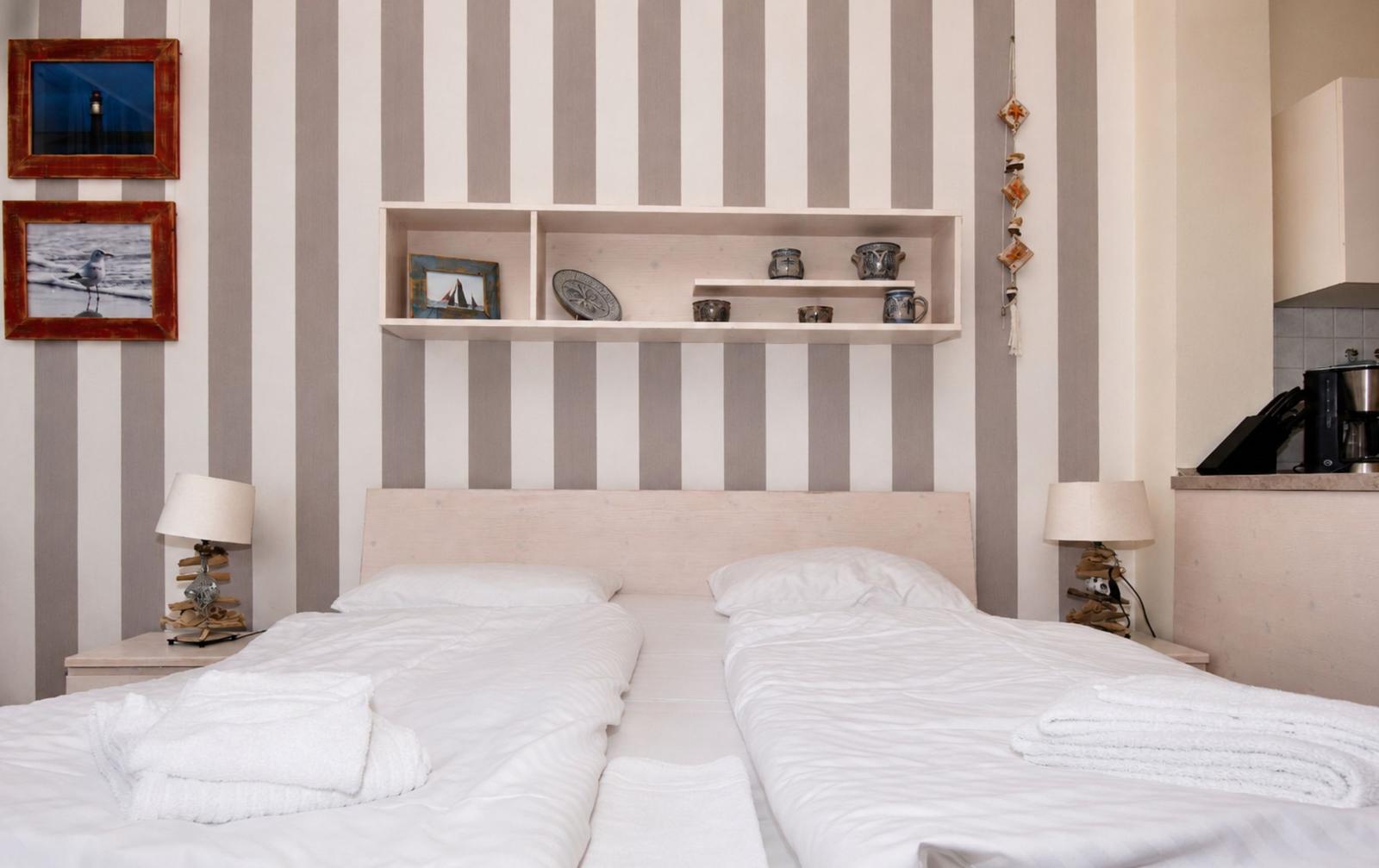 Zwei Betten mit weißen Bettwäsche, Streifenwand und Regal mit Dekoration.