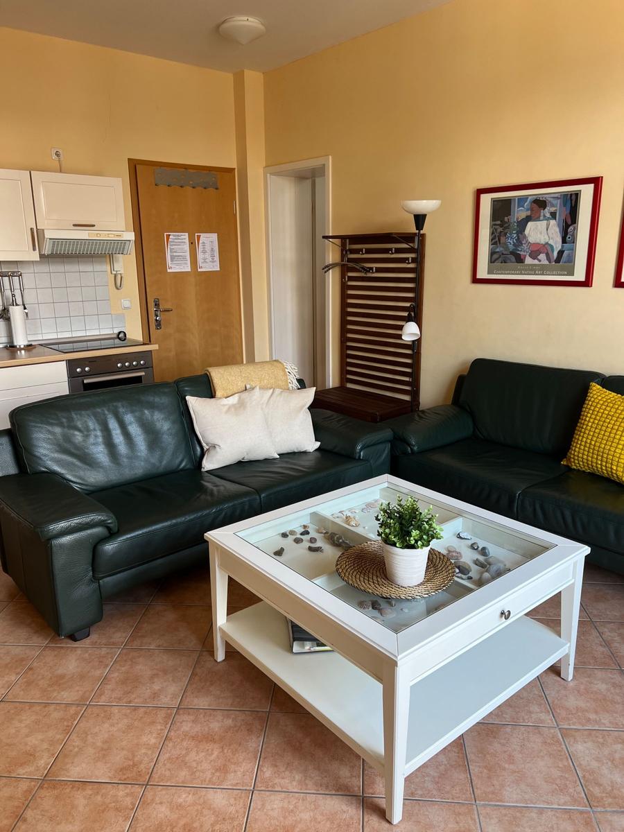 Wohnbereich mit zwei schwarzen Sofas, weißem Couchtisch und Küchenbereich.