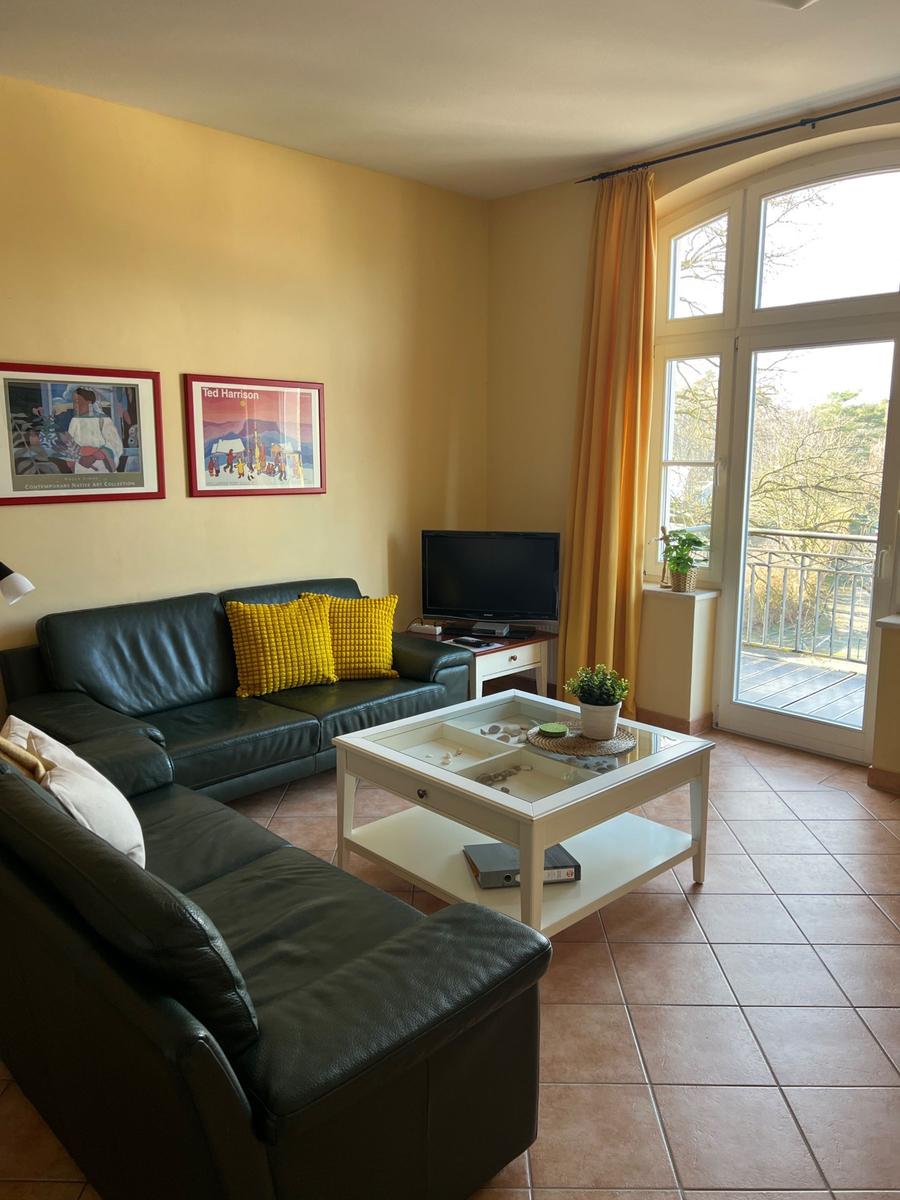 Wohnzimmer mit Ledersofa, Glas-Tisch und Blick auf Balkon.