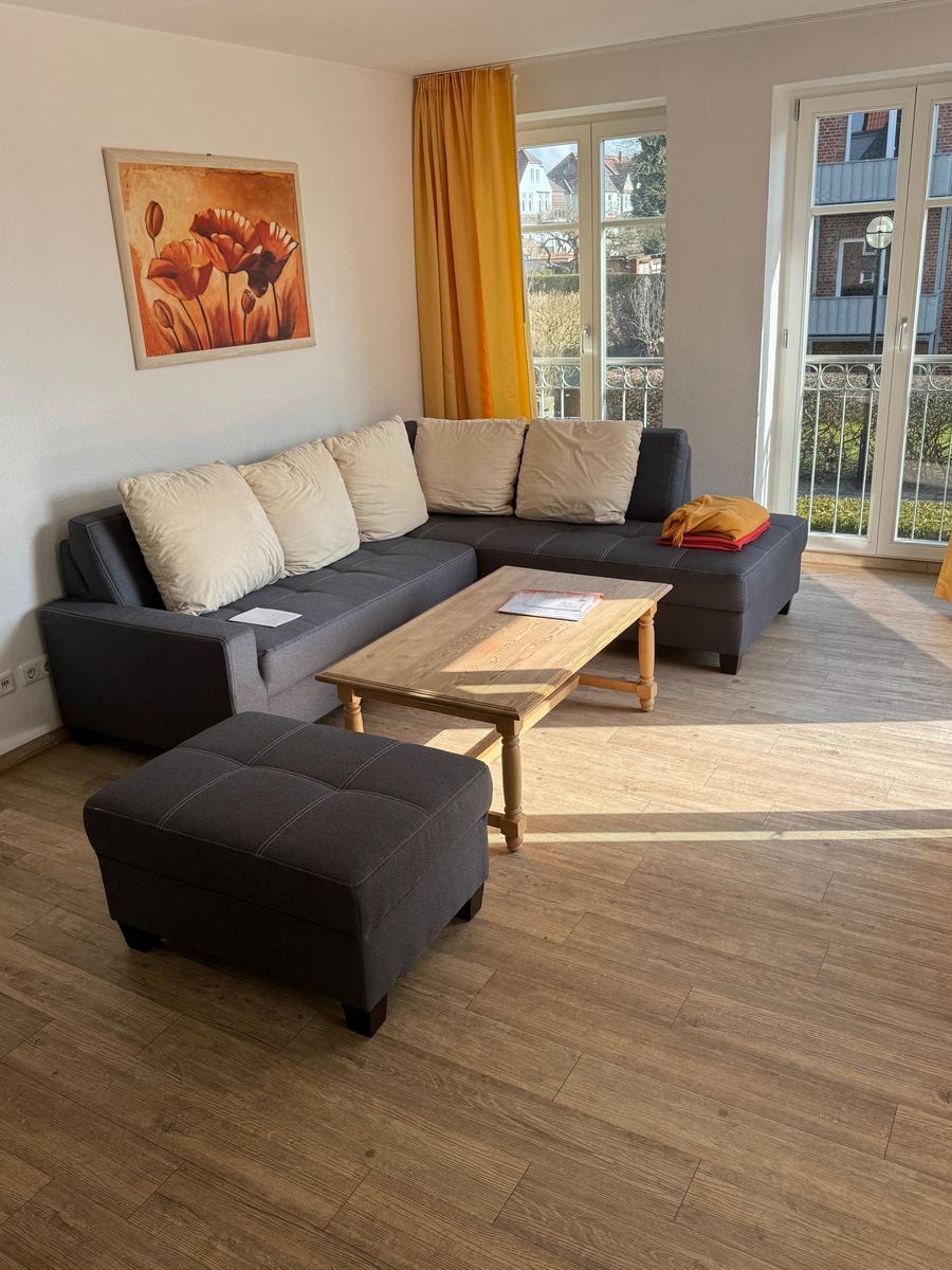 Wohnzimmer mit grauem Sofa, Holztisch und Blick auf Balkon.