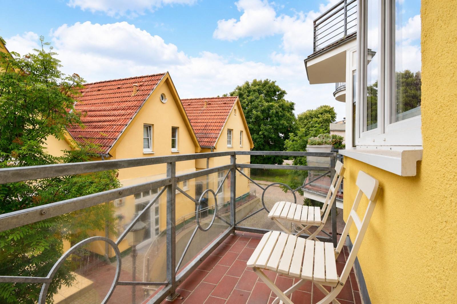 Terrasse mit zwei Stühlen, Blick auf gelbe Häuser und Bäume.