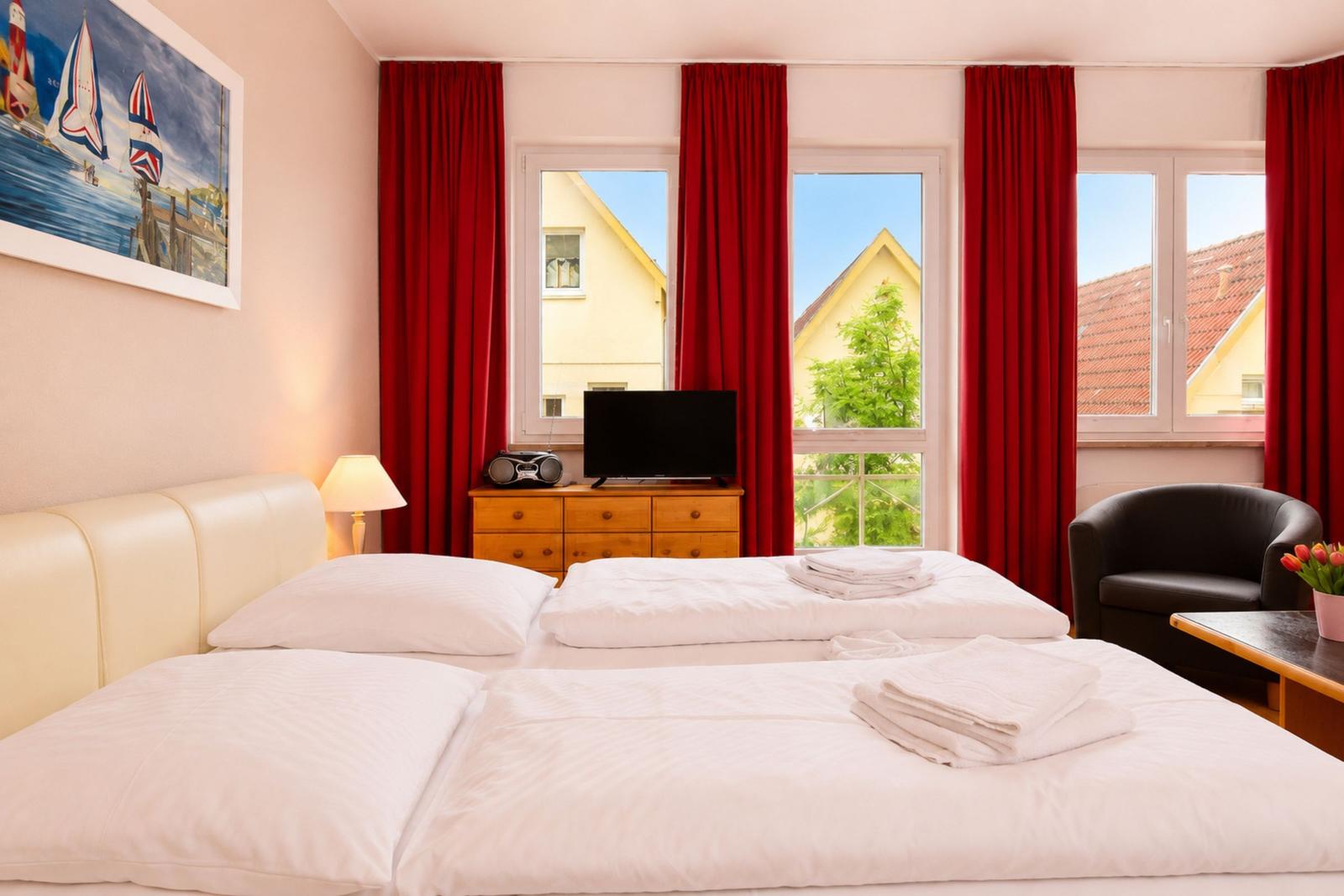 Schlafzimmer mit Doppelbett, roten Vorhängen und Blick auf Häuser.