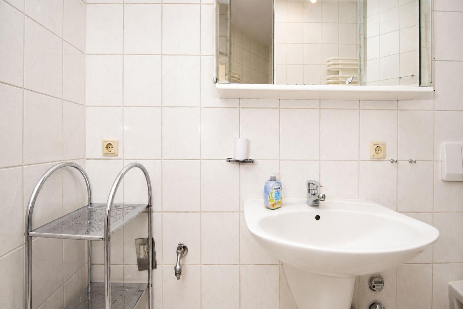 Badezimmer mit Waschbecken, Spiegel und Metallregal an der Wand.