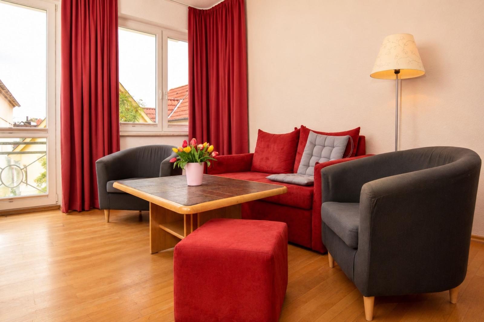 Ein Wohnzimmer mit rotem Sofa, zwei grauen Sesseln und einem Holztisch.