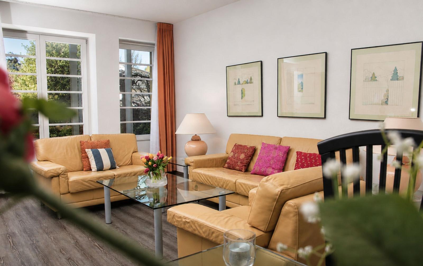 Wohnzimmer mit zwei Ledersofas, Glas-Tisch und Fenstern mit Vorhängen.
