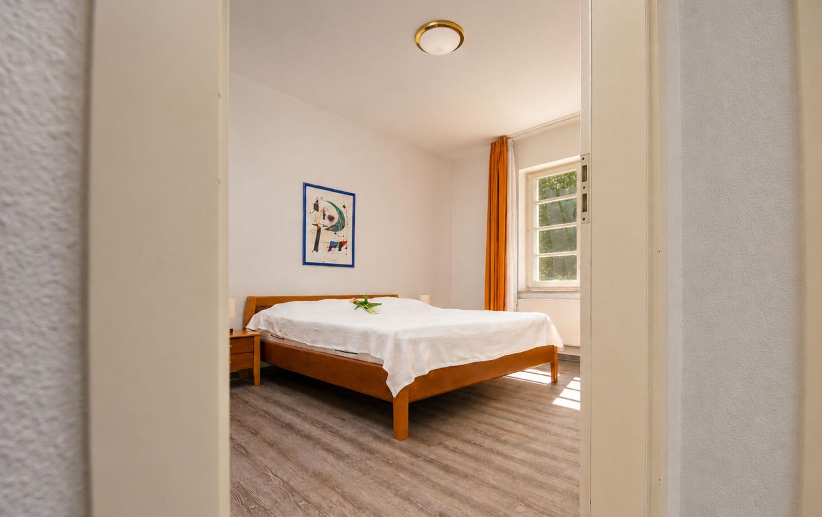 Schlafzimmer mit Holzbett, Fenster und Wandbild.
