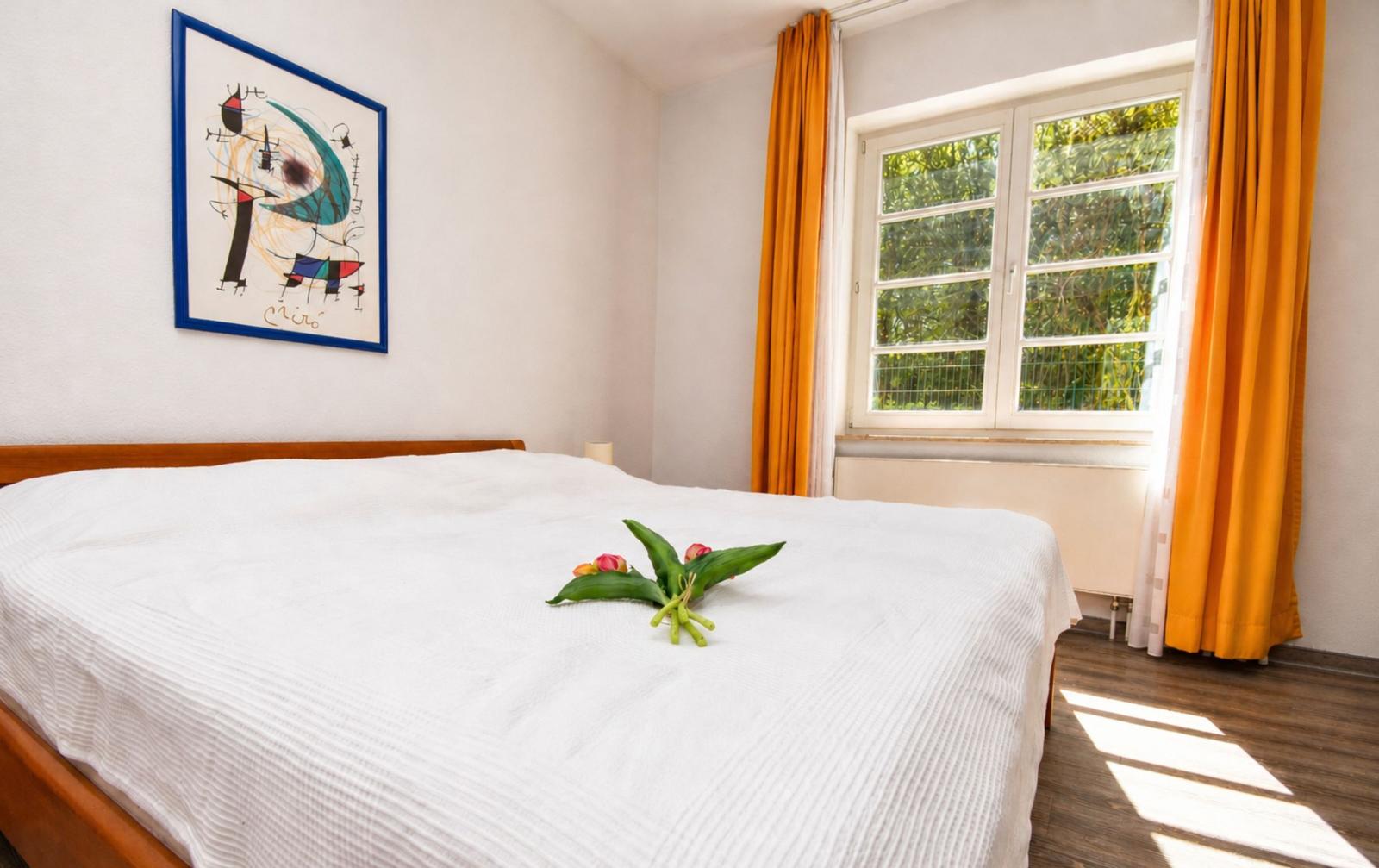 Schlafzimmer mit Bett, Fenster und Wandbild.