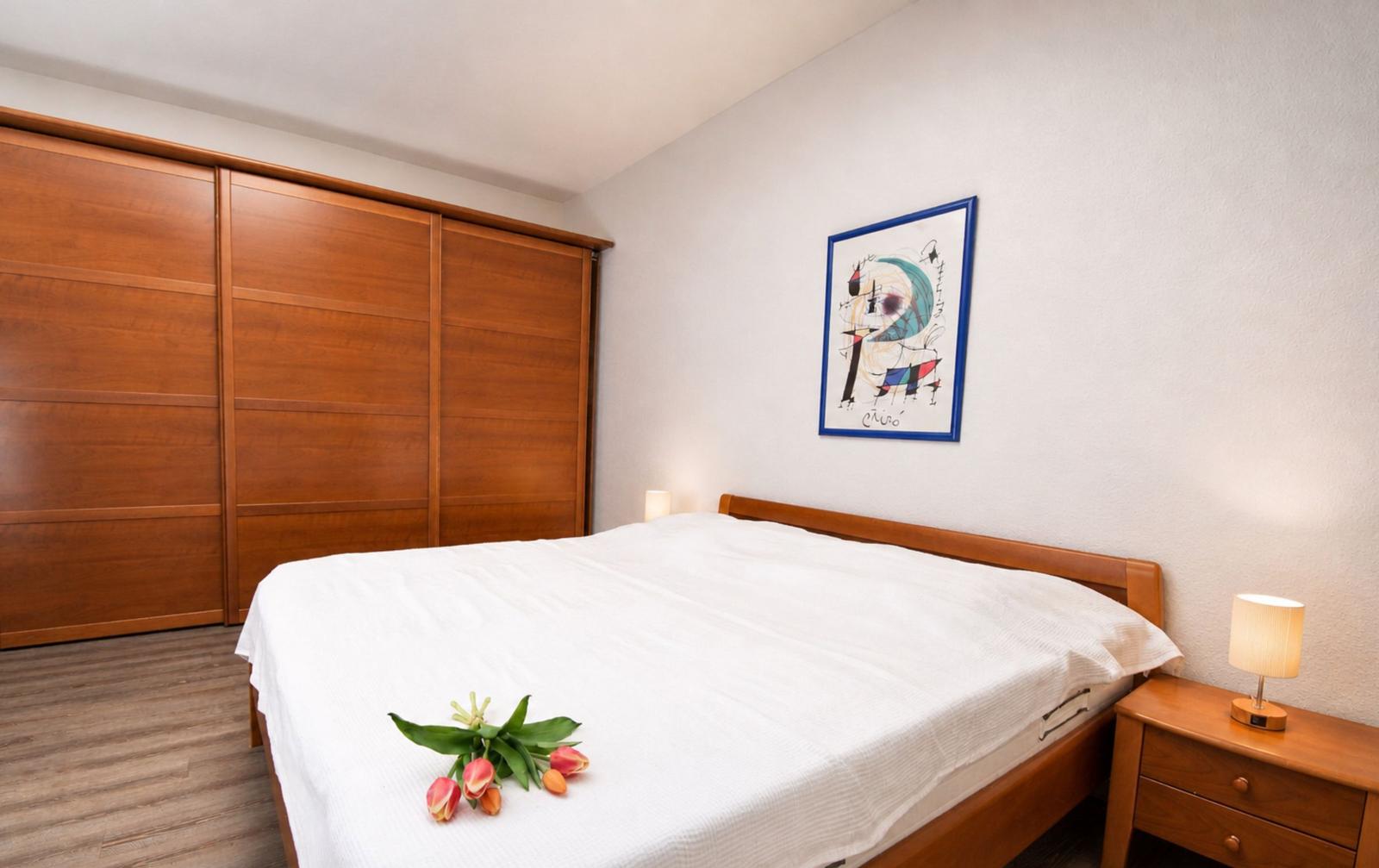 Schlafzimmer mit Bett, Schrank und Nachttisch. Auf dem Bett liegen Blumen.