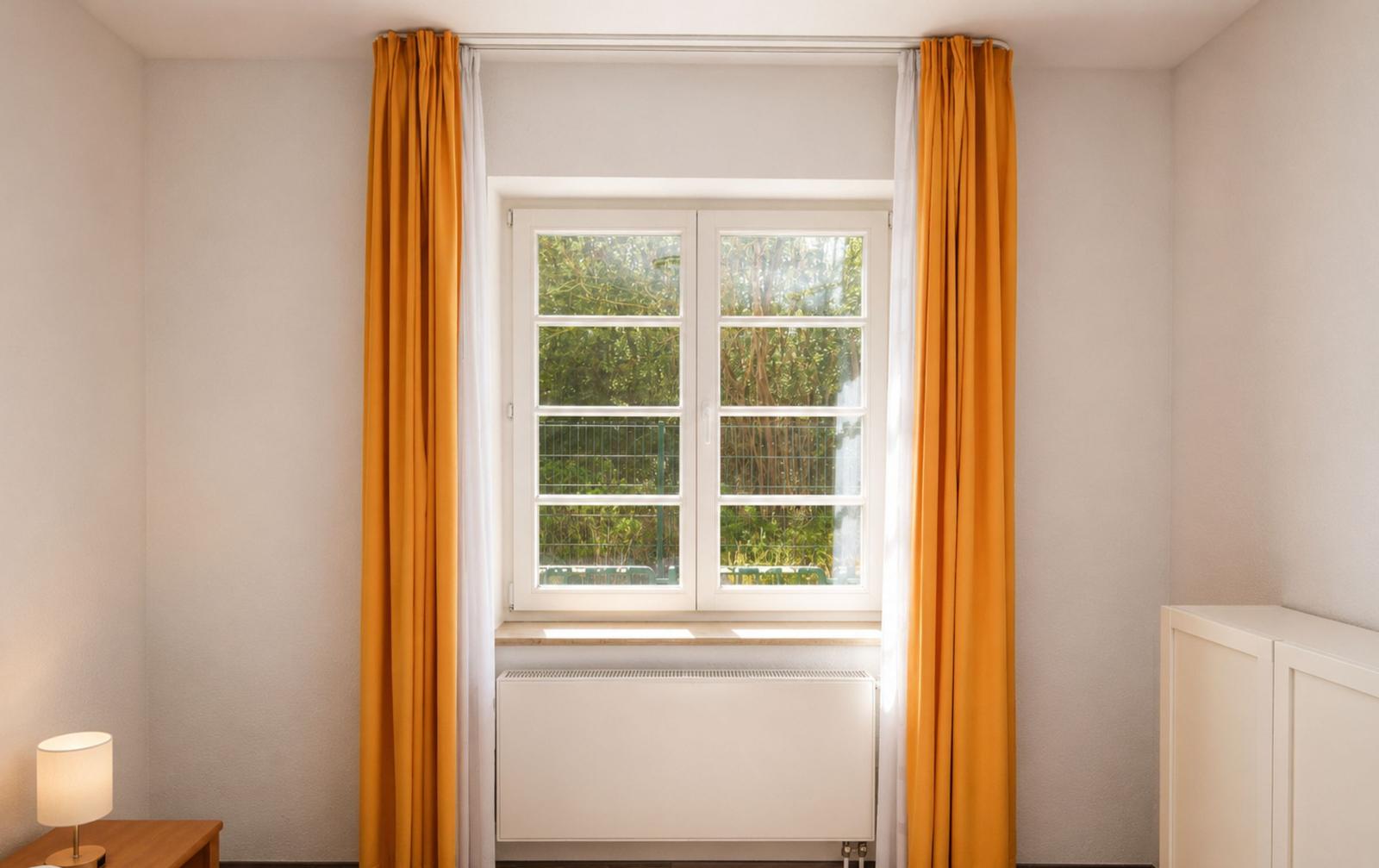 Zimmer mit Fenster, orangefarbenen Vorhängen und weißem Heizkörper.