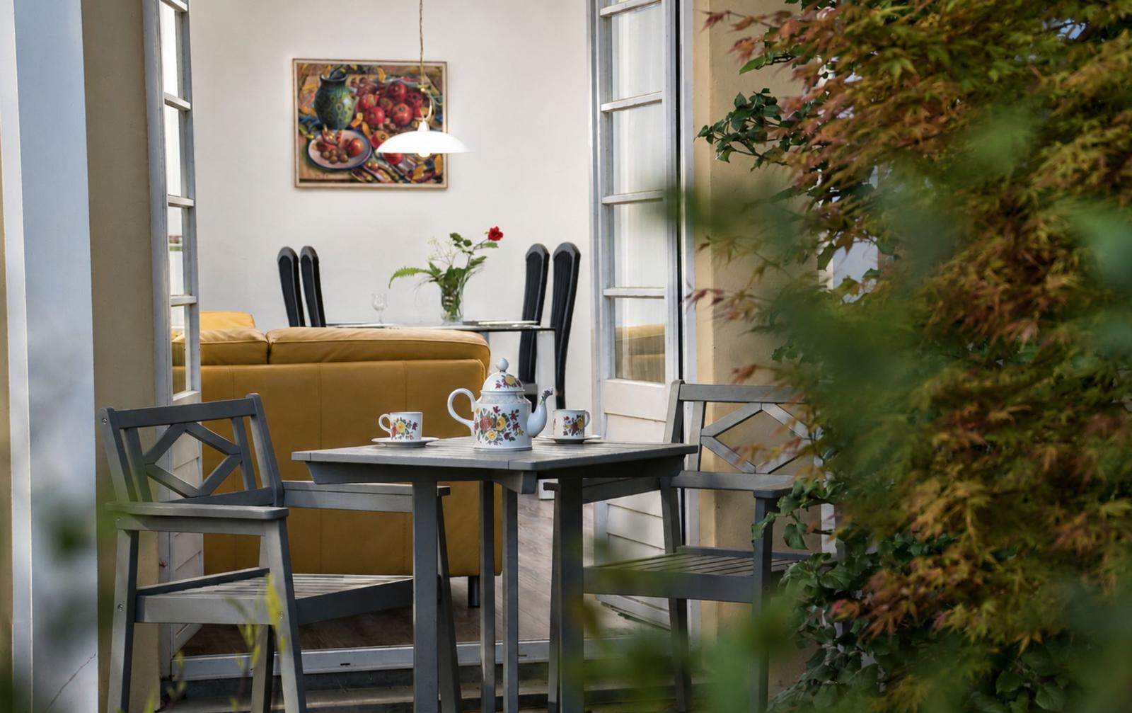 Terrasse mit Tisch und Stühlen, Blick ins Haus mit Sofa und Wandbild.