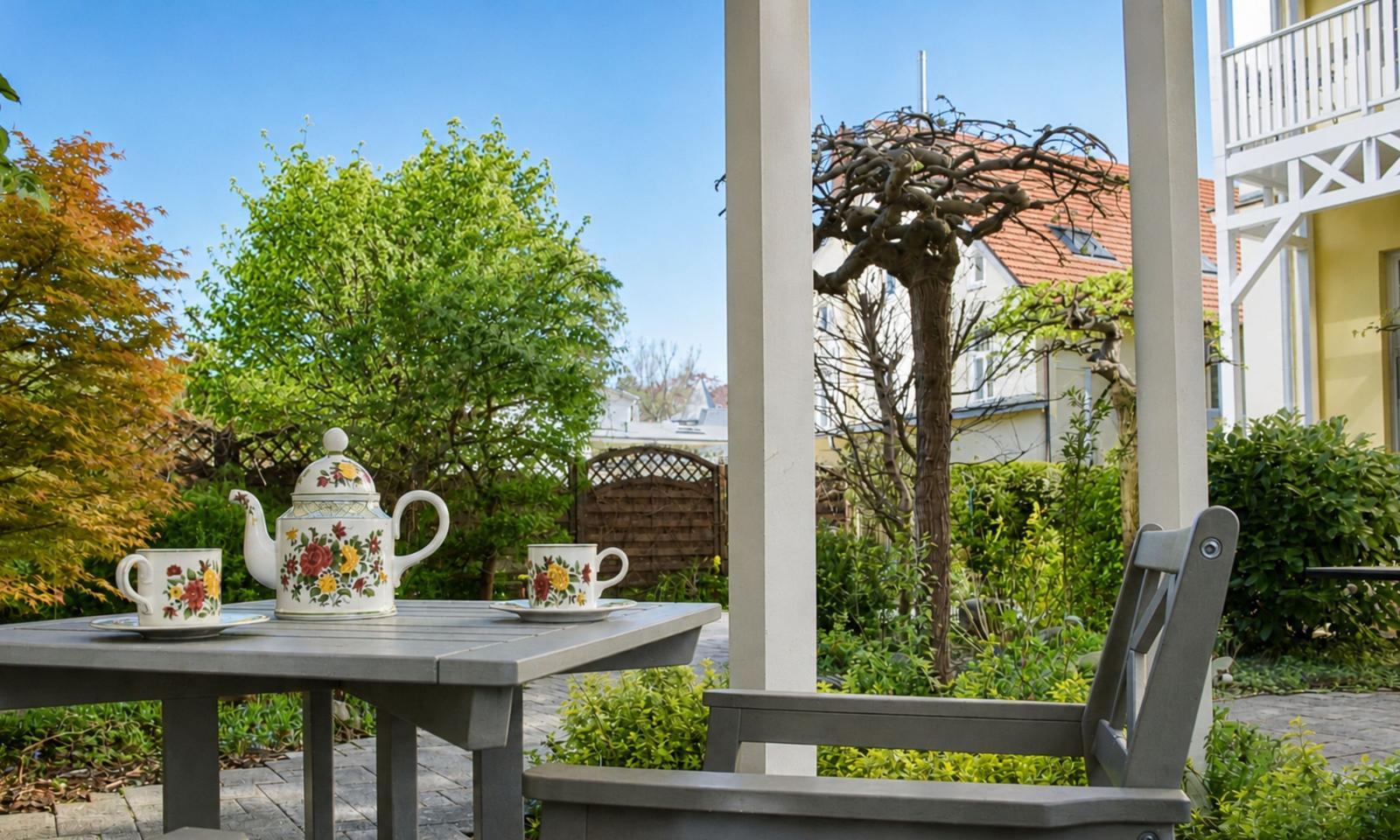 Tisch mit Teekanne und Tassen unter Pavillon im Garten. Blick auf Hinterhof und Nachbarhaus.
