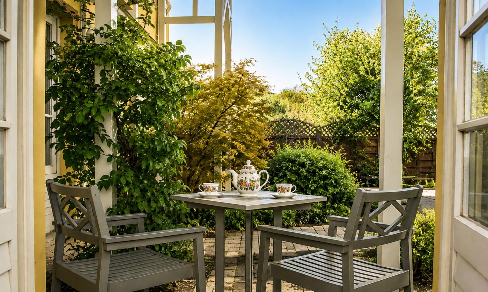 Auf der Terrasse steht ein Tisch mit zwei Stühlen und einer Teekanne mit Tassen.
