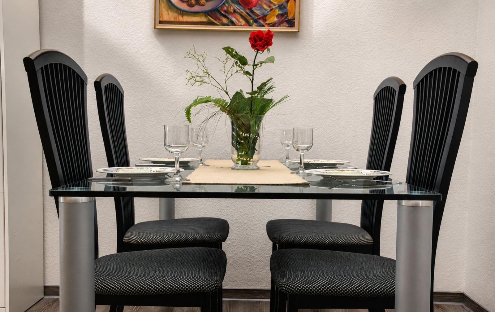 Esstisch mit vier Stühlen, Blumenvase und Gemälde an der Wand.