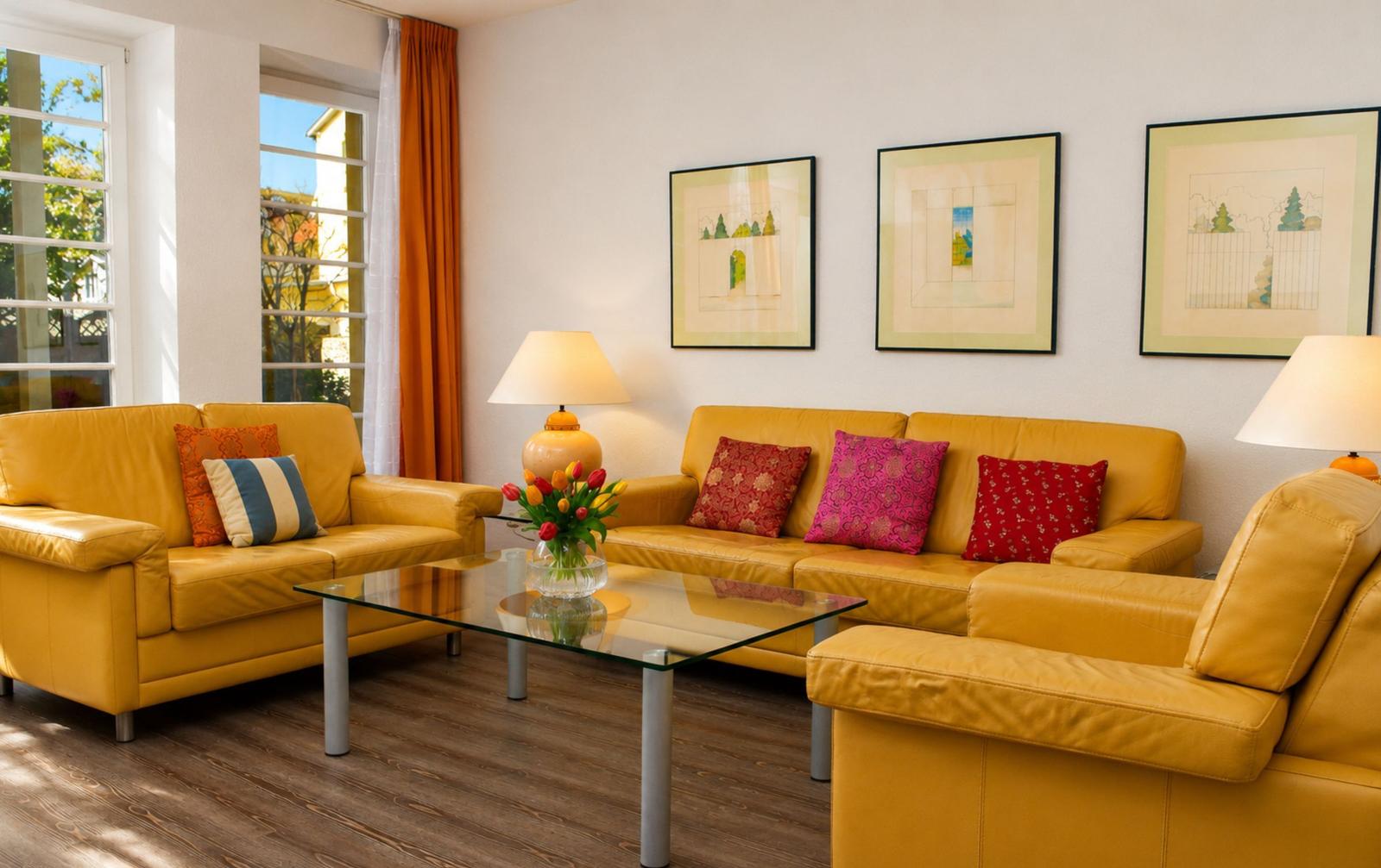 Wohnzimmer mit gelben Ledersofas, Glas-Tisch und Fenstern mit orangefarbenen Vorhängen.