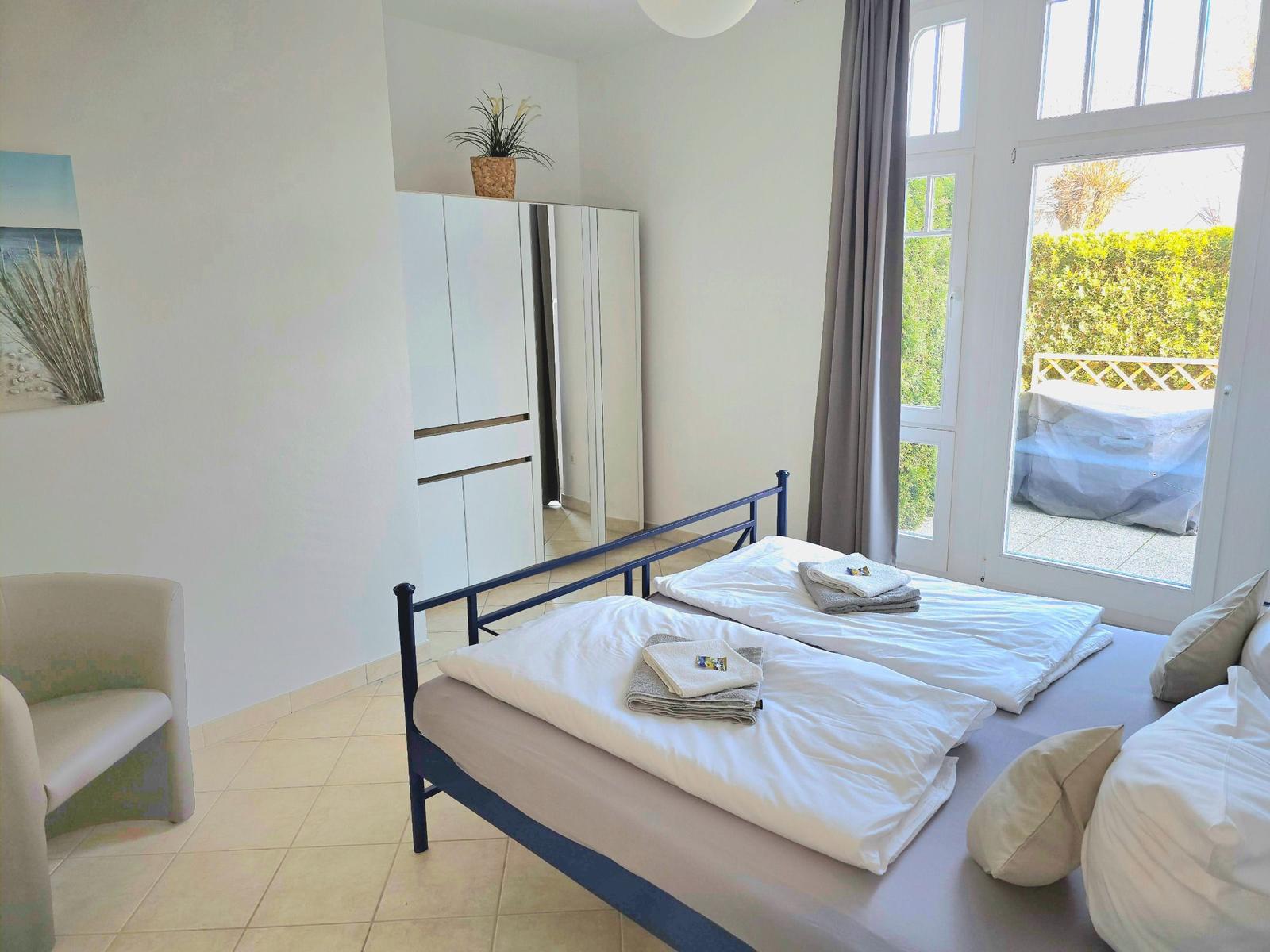Schlafzimmer mit Doppelbett, Schrank und Blick auf Balkon.