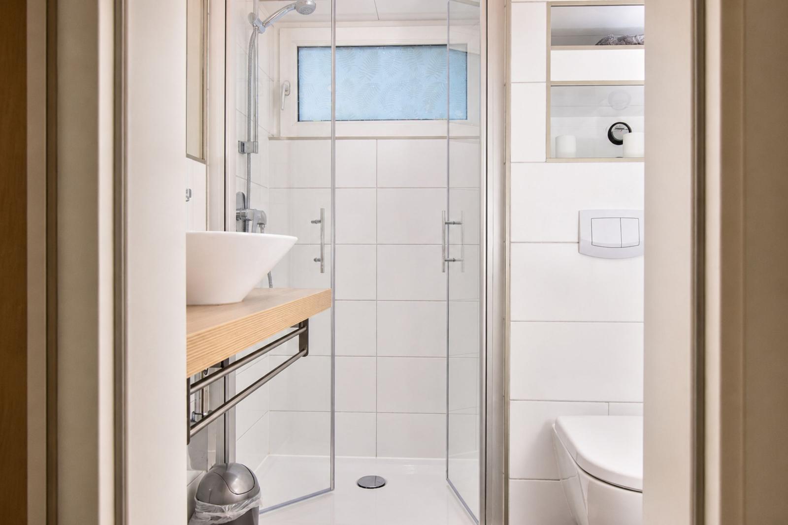 Badezimmer mit Dusche, Waschbecken und Toilette. Weiße Fliesen und Holzunterschrank.
