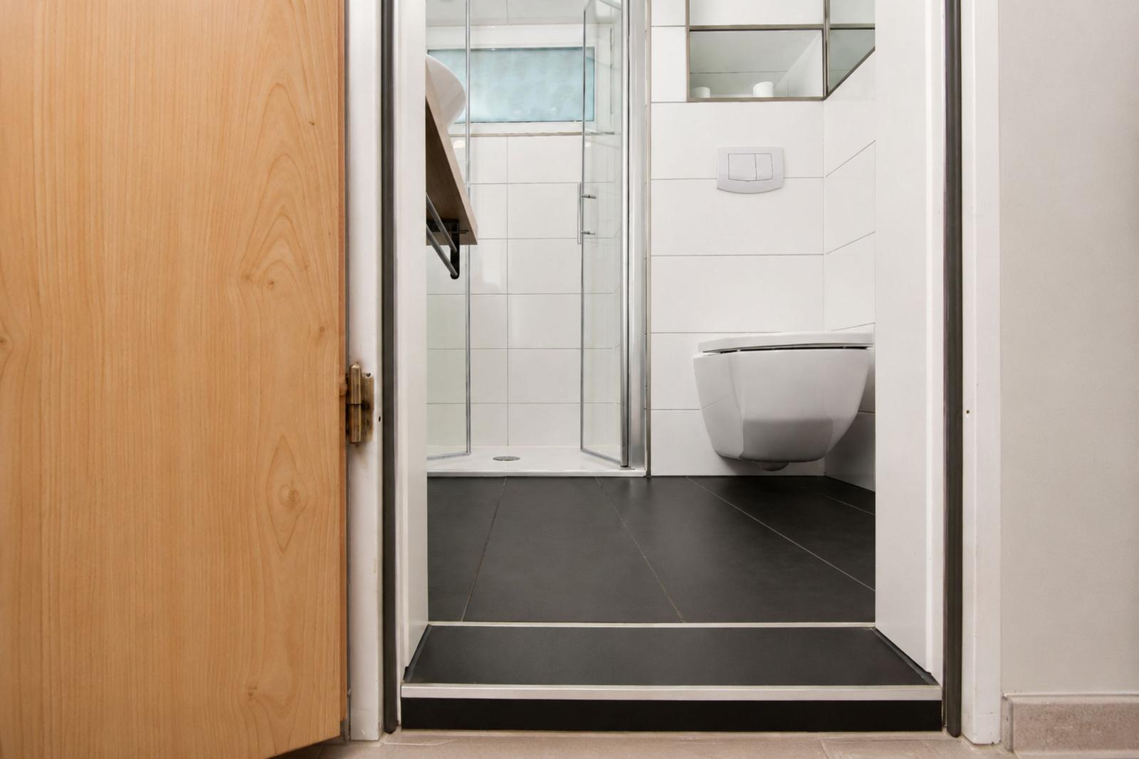 Badezimmer mit Dusche, WC und schwarzem Bodenbelag.