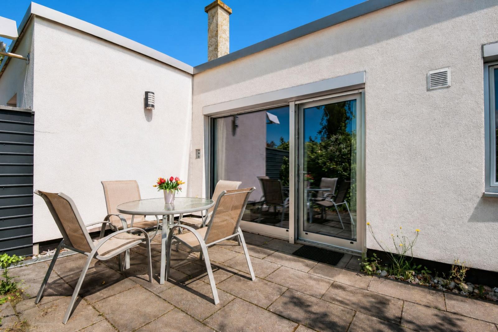Terrasse mit Tisch und Stühlen, Schiebetür und Ziegelsteinboden.
