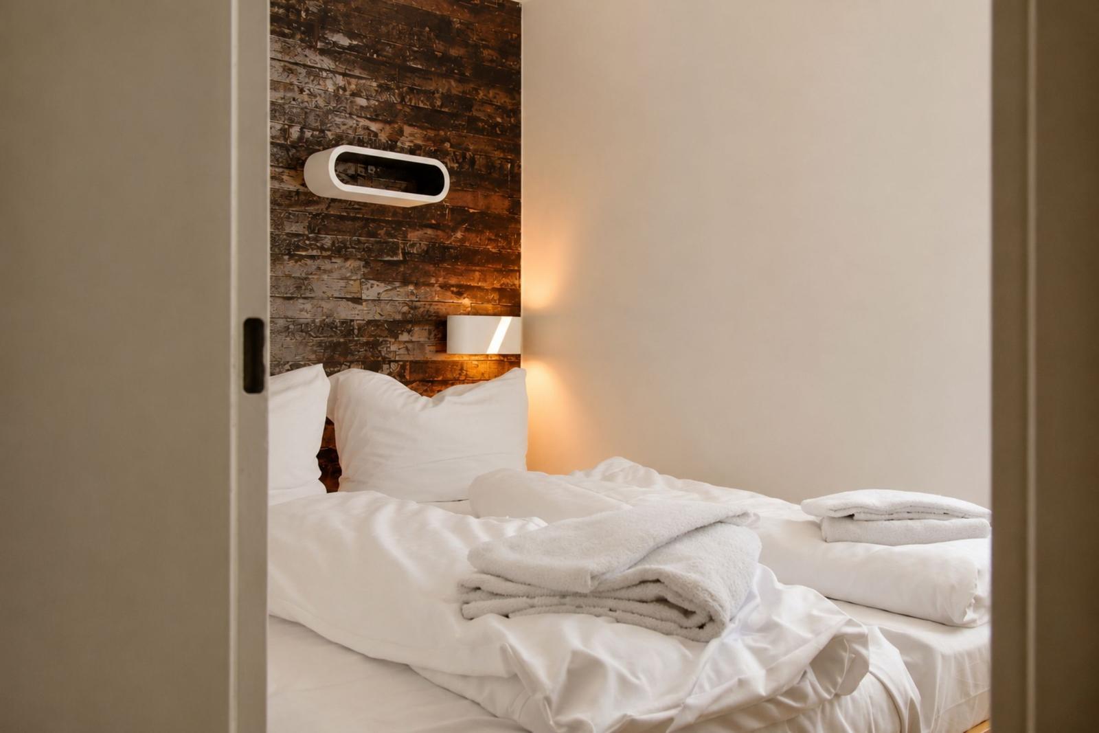 Schlafzimmer mit Bett, weißen Bettwäsche und Holzwand im Hintergrund.