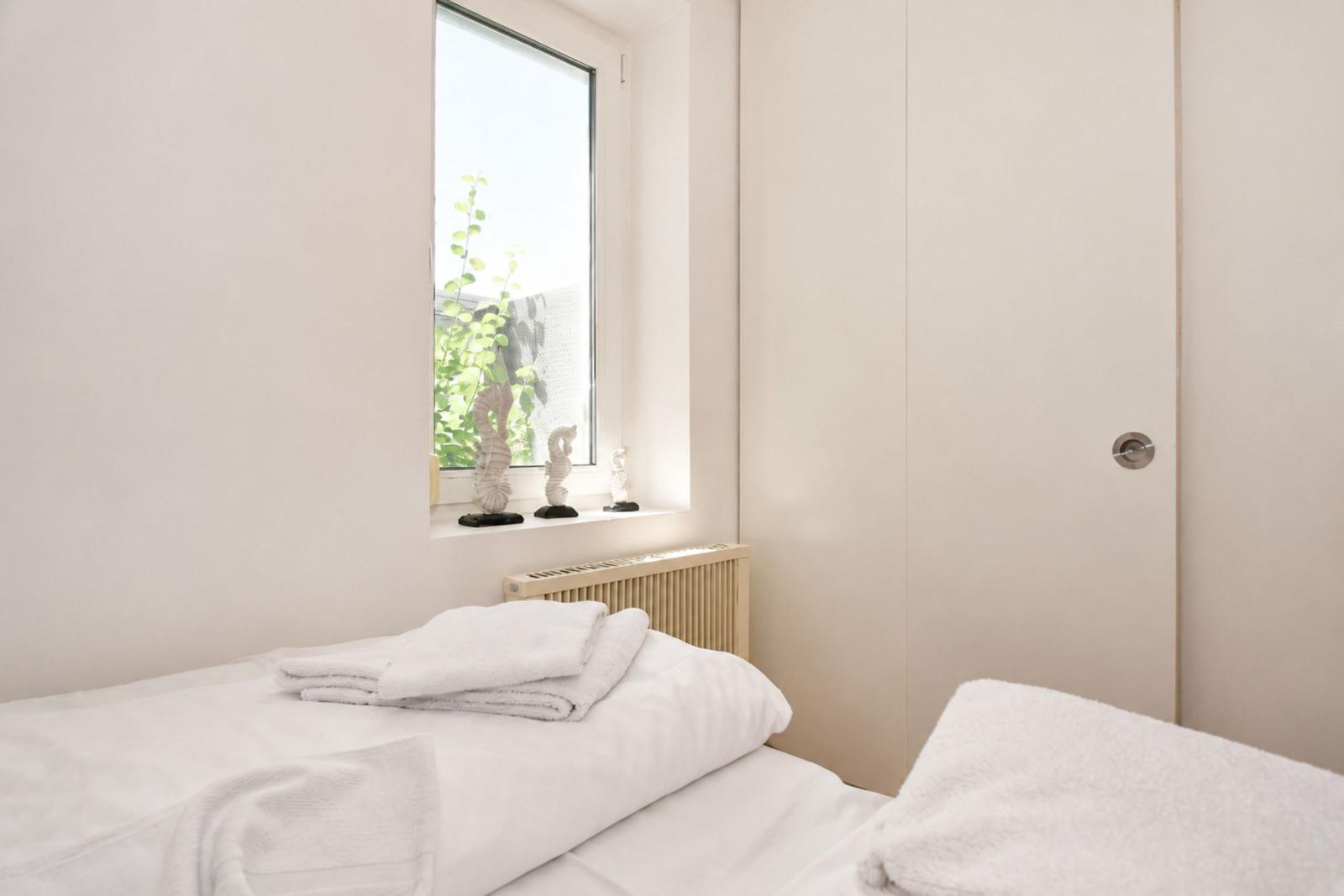 Ein Schlafzimmer mit Bett, Fenster und Kleiderschrank. Auf dem Fensterbrett stehen weiße Figuren.