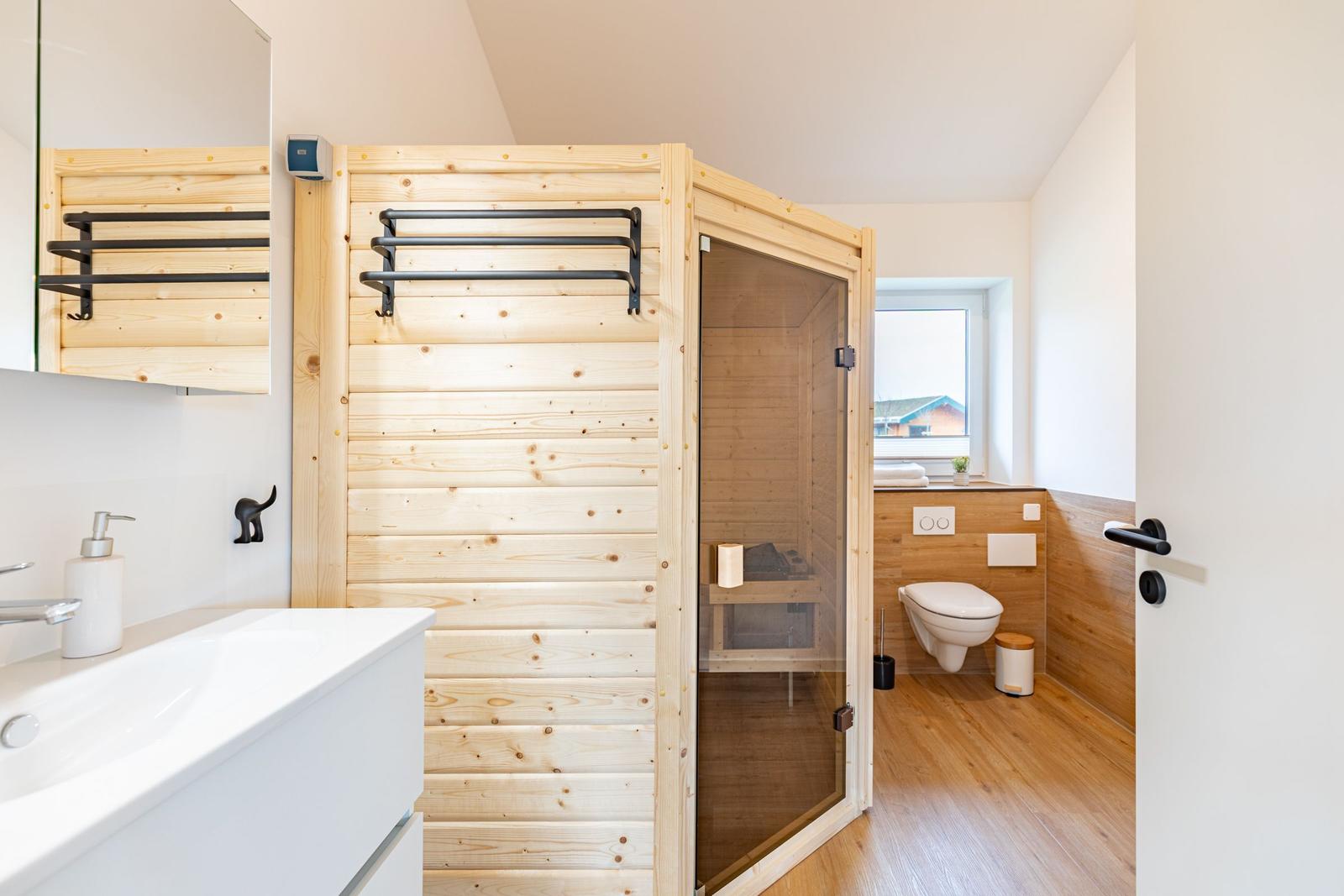 Bad mit Sauna, Waschbecken und Toilette. Holzwände und Fensterblick.