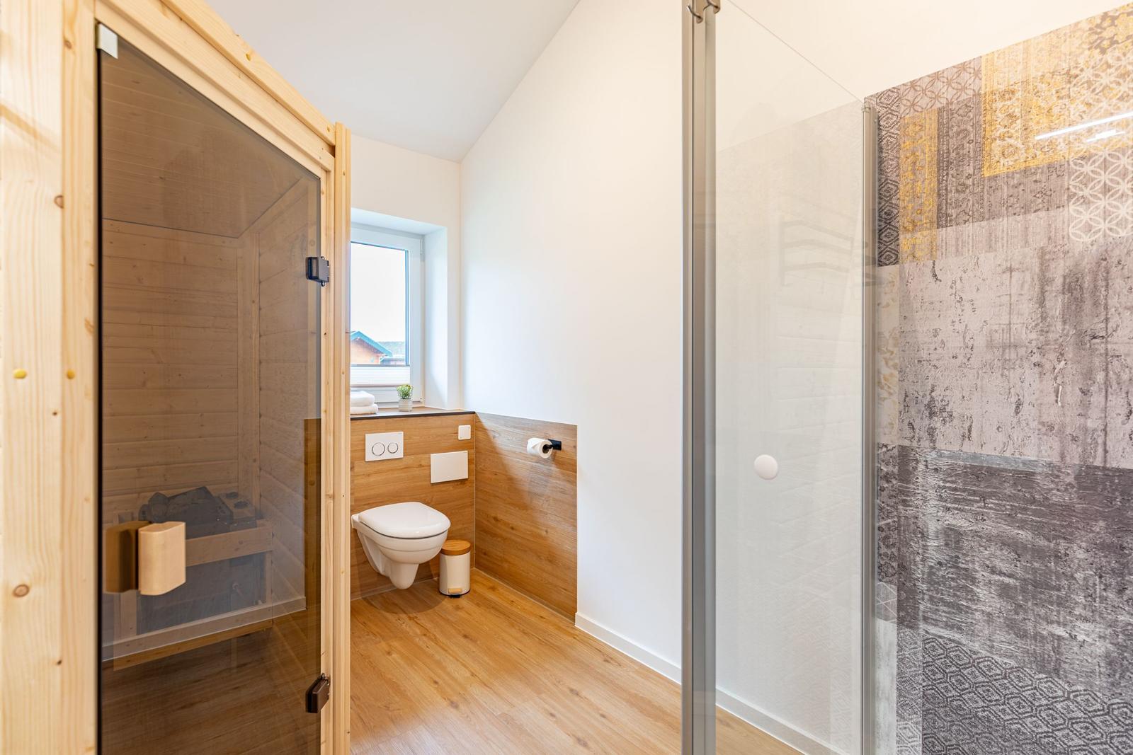 Bad mit Dusche, Toilette und Sauna. Holzfußboden und Fenster mit Blick.