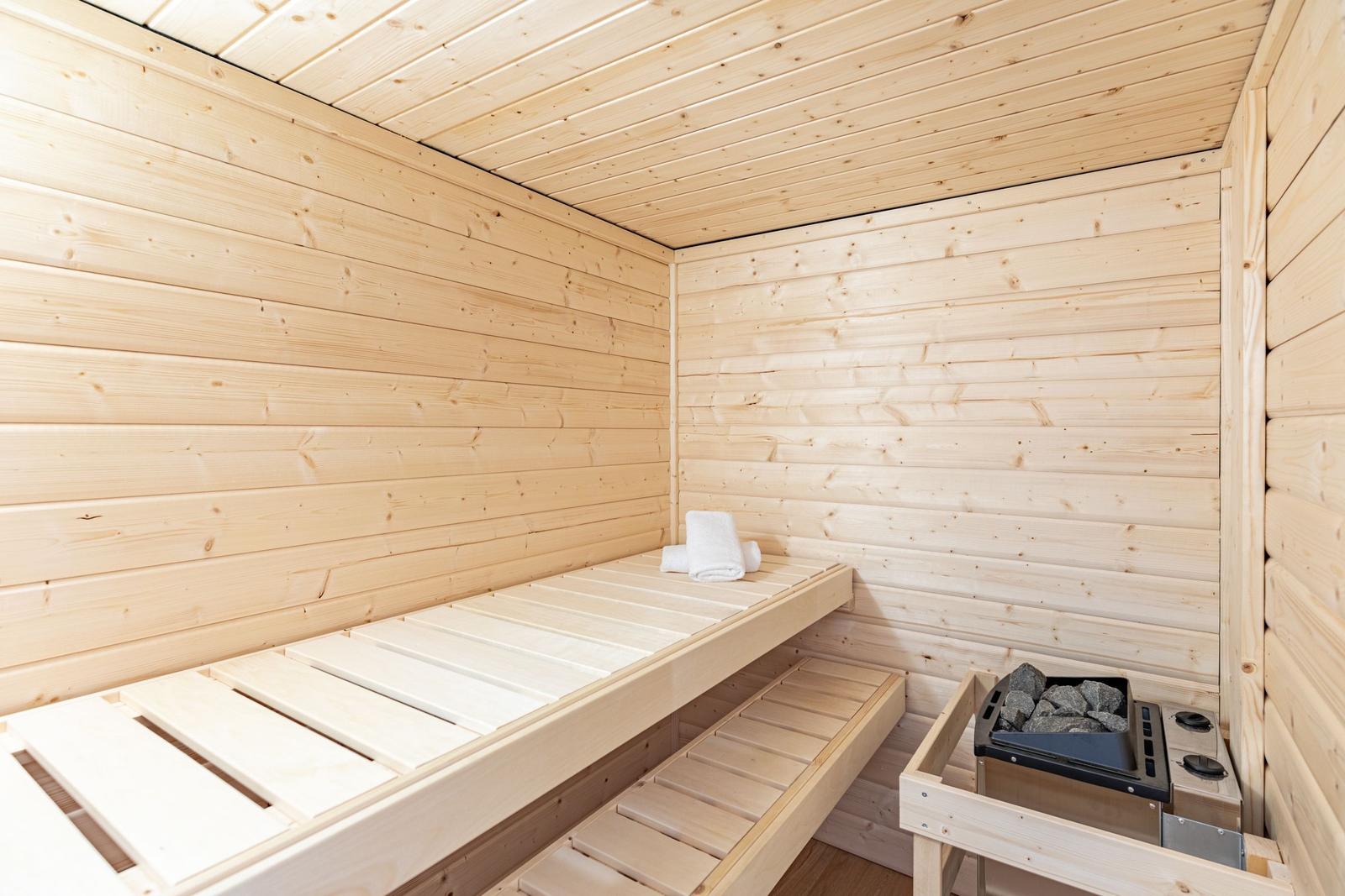 Sauna mit Holzwand, Sitzbank und Heizung mit Steinen.