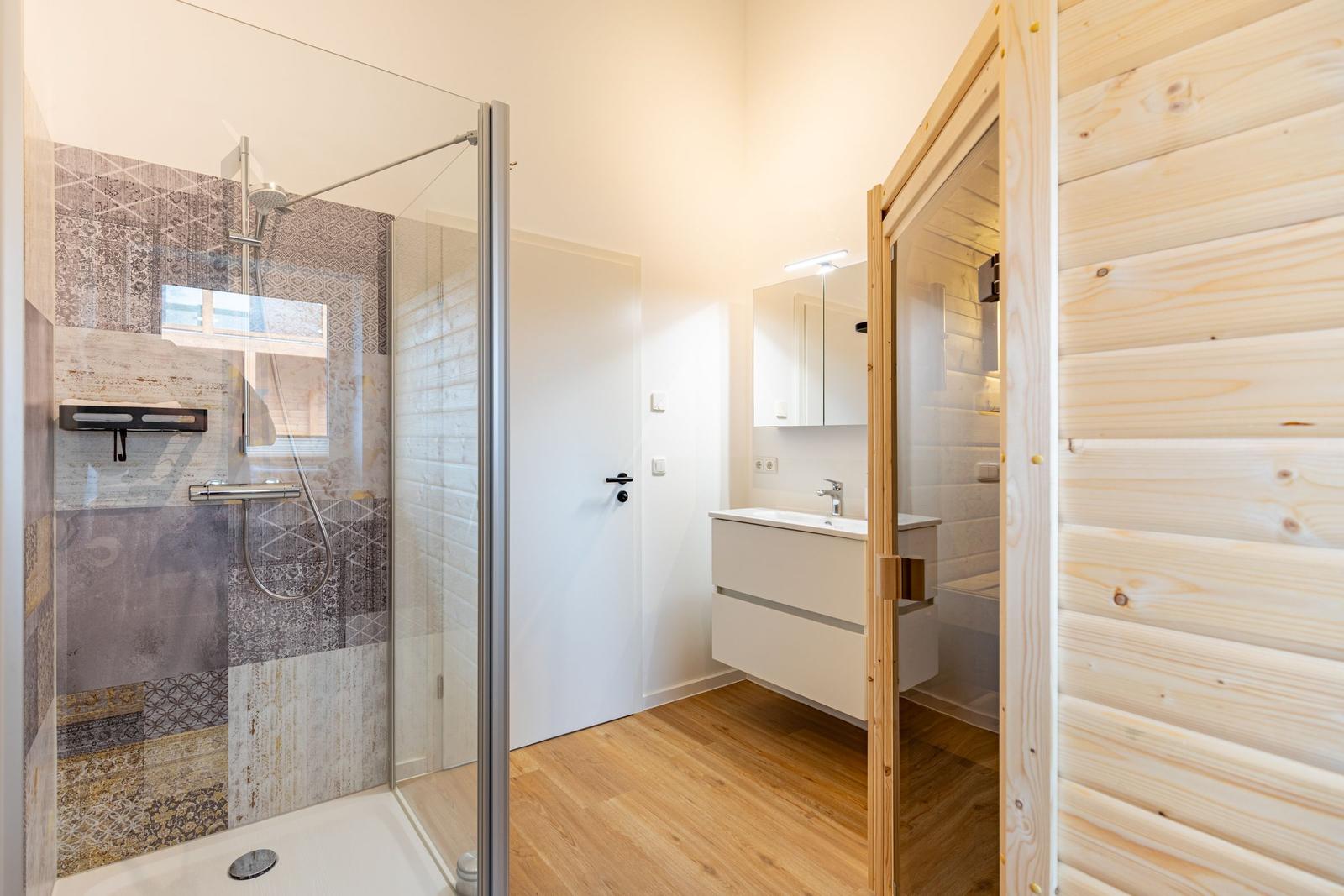 Bad mit Dusche, Waschbecken und Holzsauna.