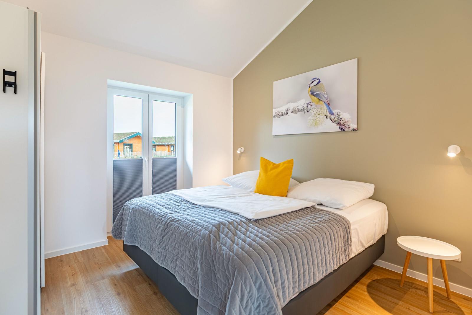 Schlafzimmer mit Bett, Wandbild und Fenster. Holzboden und Nachttisch.