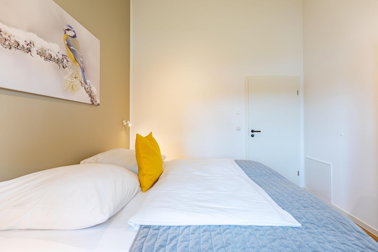 Schlafzimmer mit Bett, Kissen und Wandbild eines Vogels.