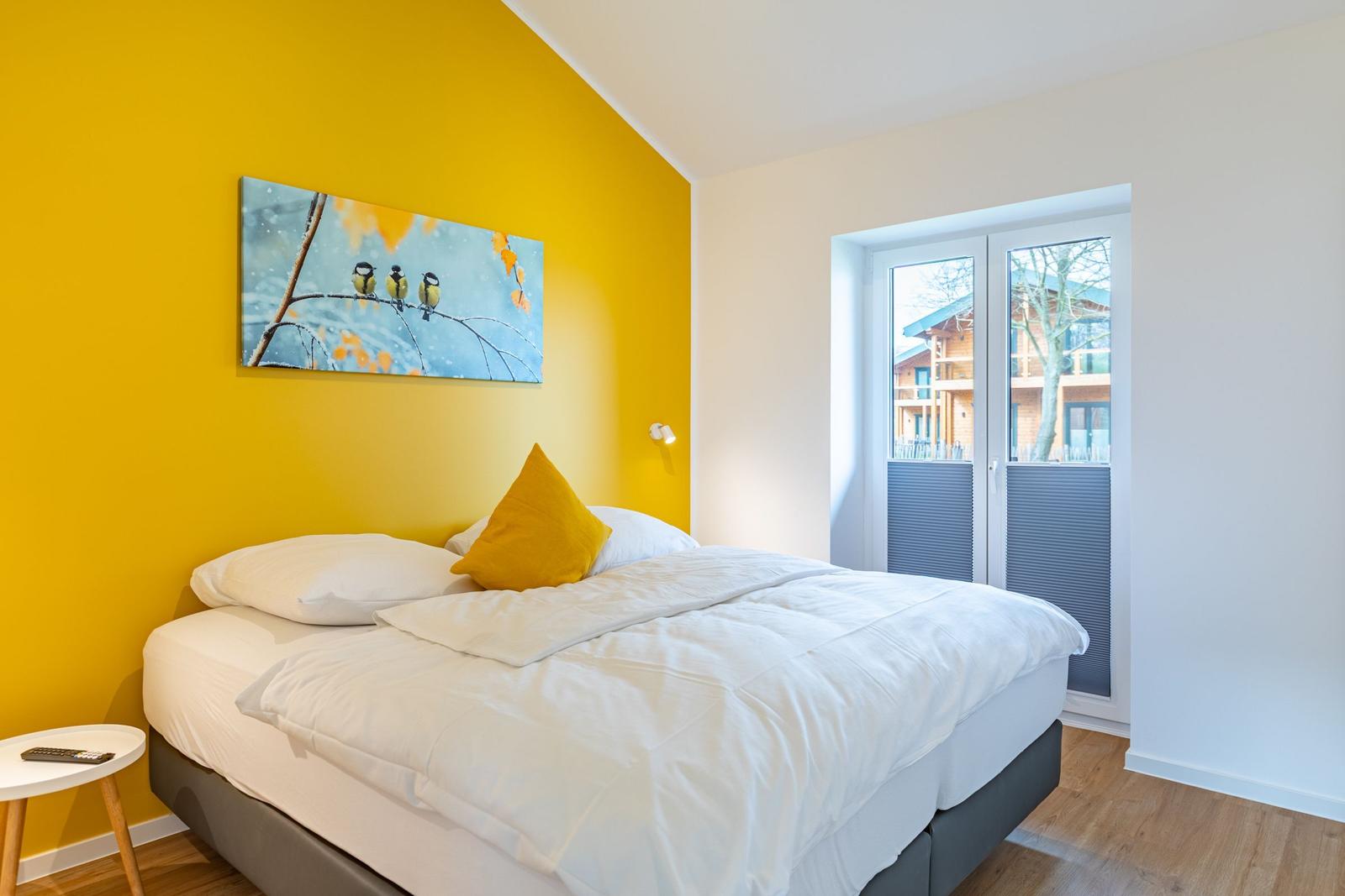 Schlafzimmer mit gelber Wand, Bett und Fenster zur Aussicht.